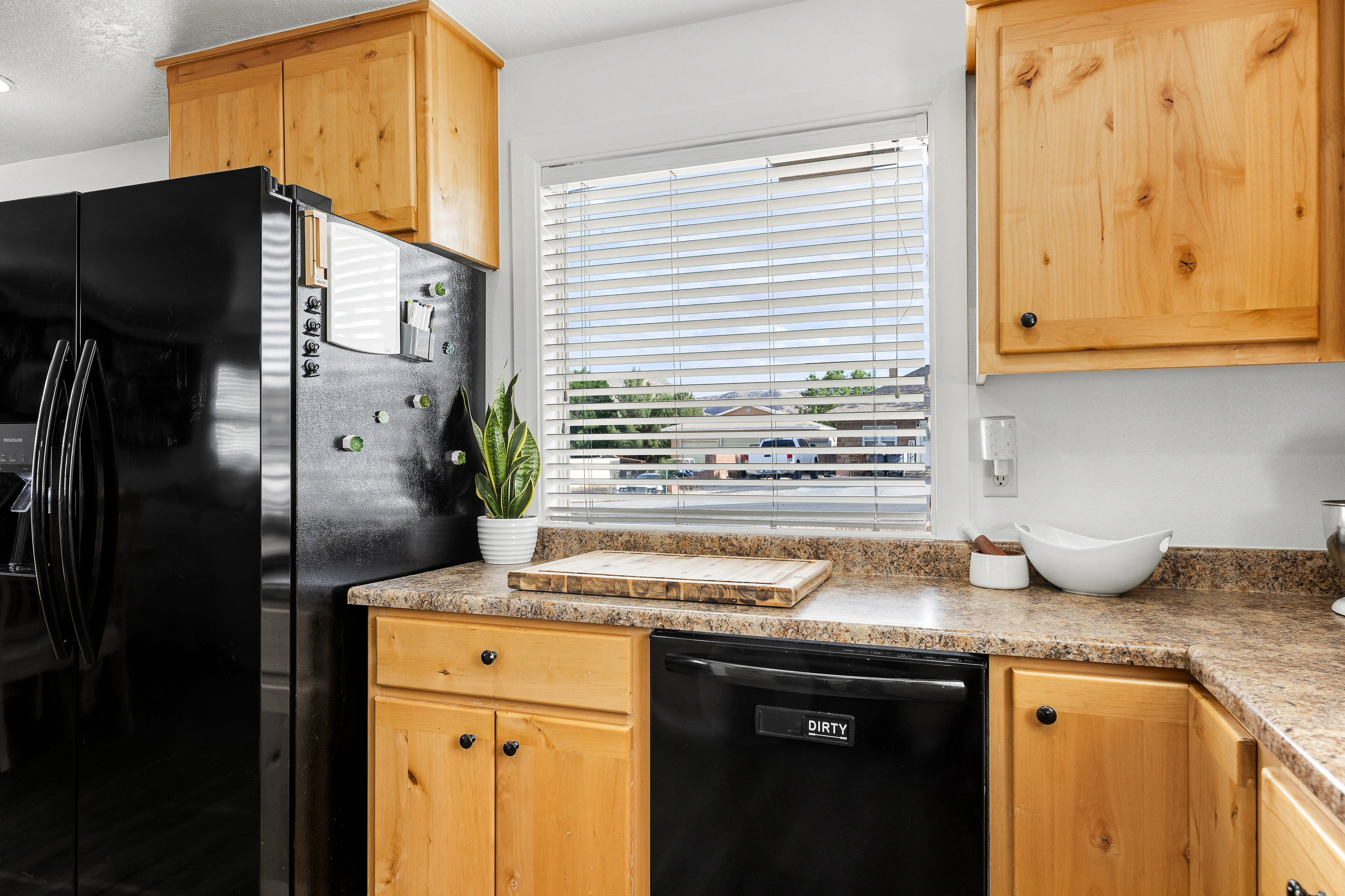 Kitchen featuring wood-finish cabinetry with black hardware, laminate countertops, a built-in dishwasher, and a window with blinds