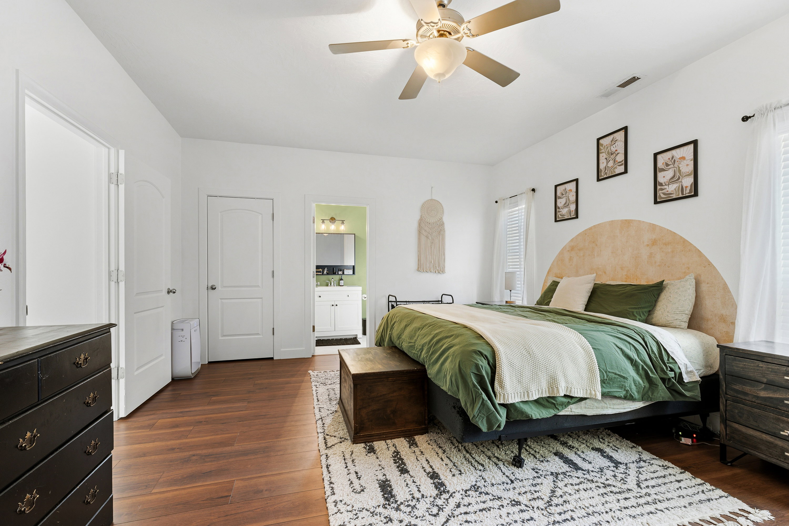Spacious bedroom featuring wood-finish flooring, white walls, and a ceiling fan with integrated lighting