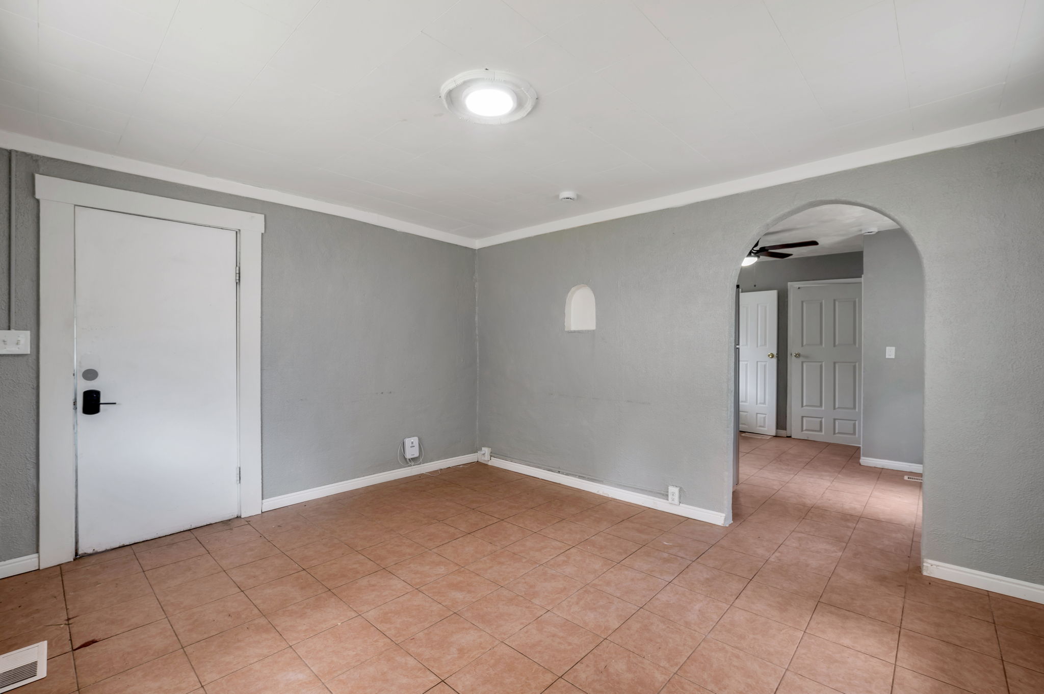 Room featuring light gray walls, white trim, terracotta-style floor tiling, an arched doorway, and a ceiling-mounted light fixture