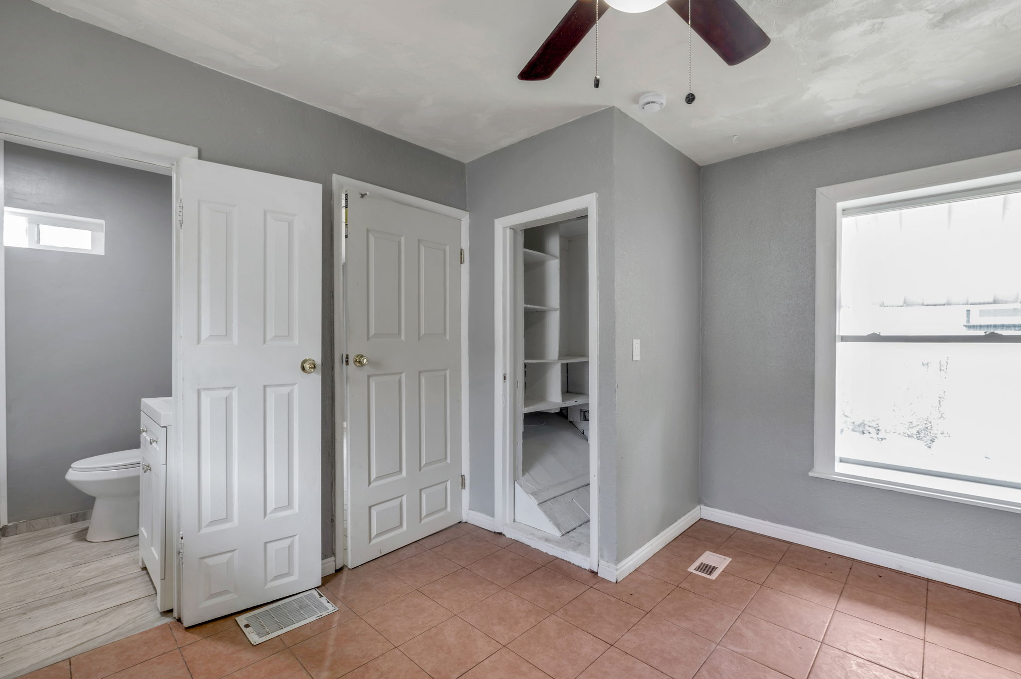 Room featuring neutral gray walls, tiled flooring, a ceiling fan, and a built-in shelving unit