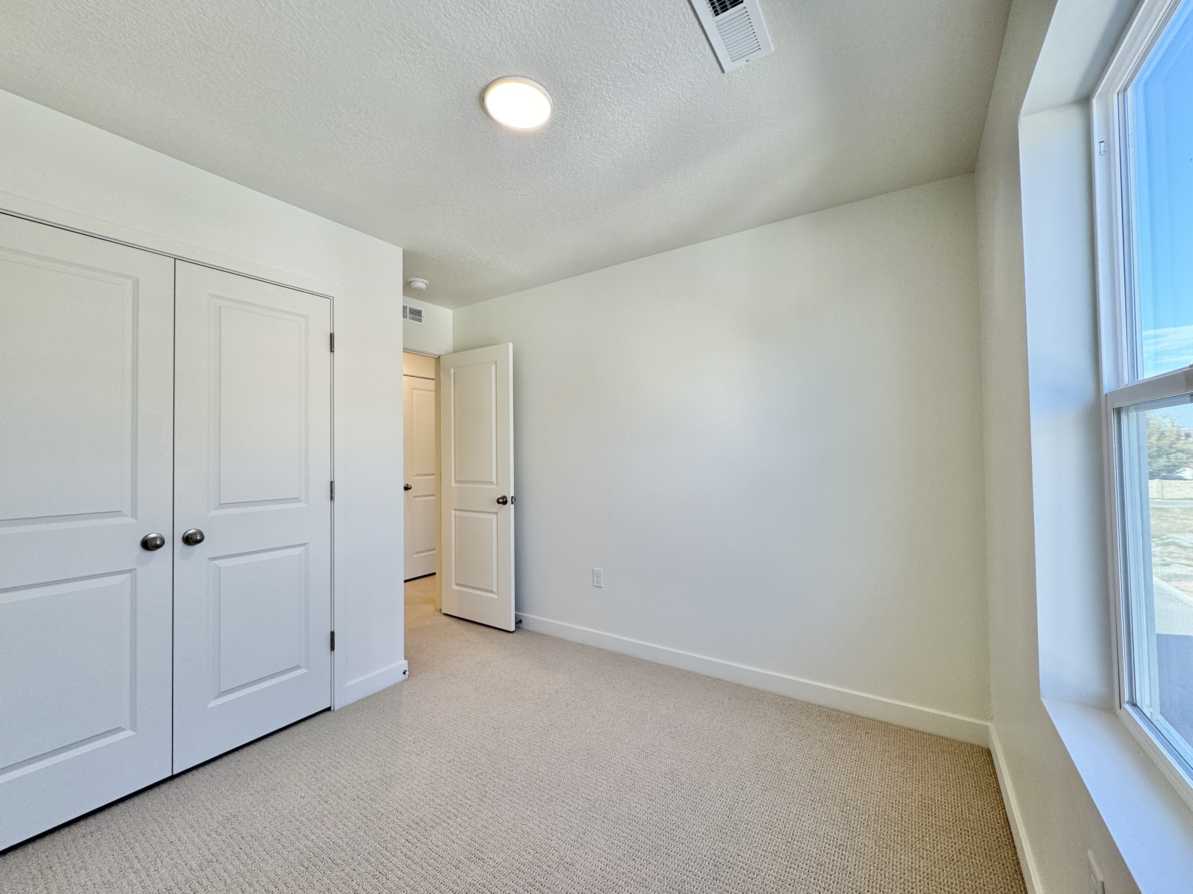 Carpeted room with white walls, a large window, a ceiling light fixture, and double bi-fold closet doors