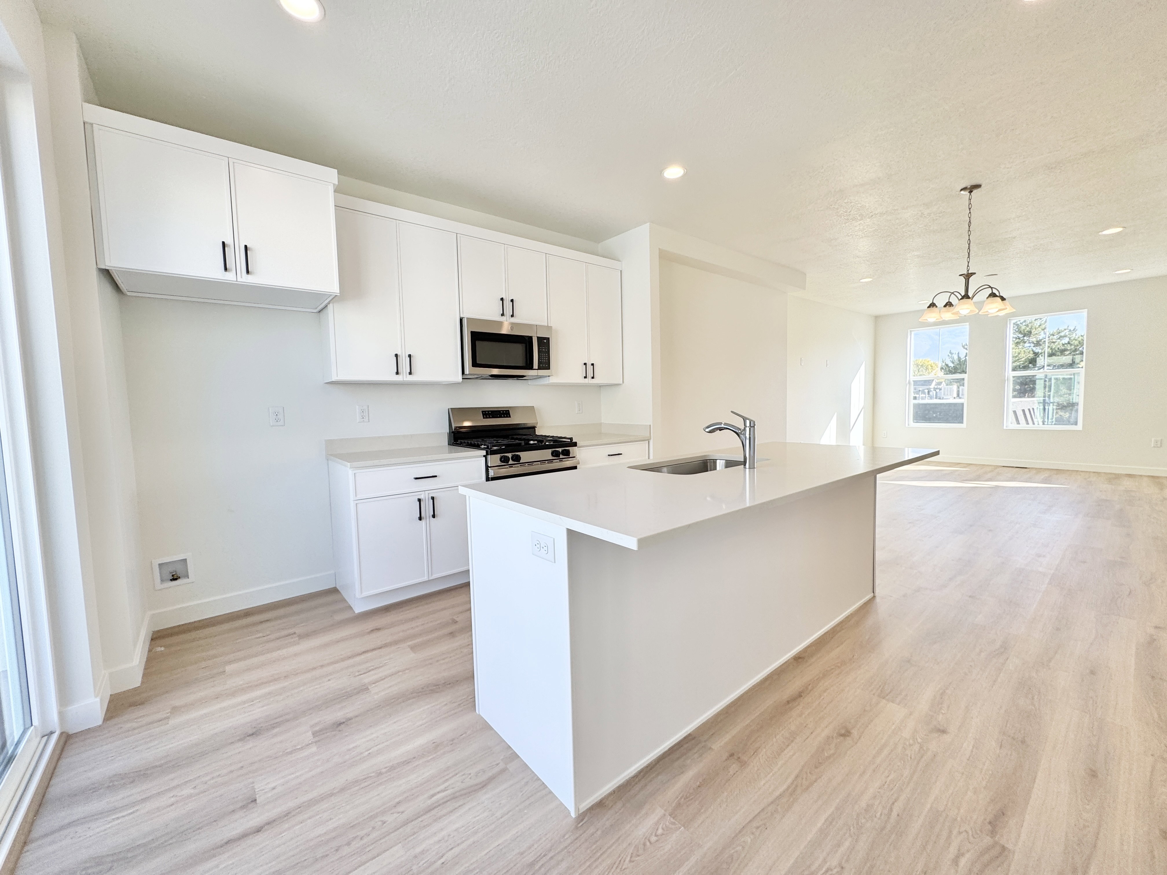 Open-concept kitchen featuring white cabinetry, stainless steel appliances, a center island with an undermount sink, and light wood-finish flooring extending into the dining area
