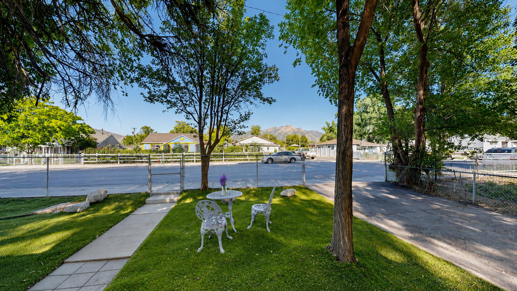 Manicured front yard featuring a paved walkway, mature trees, and a chain-link fence