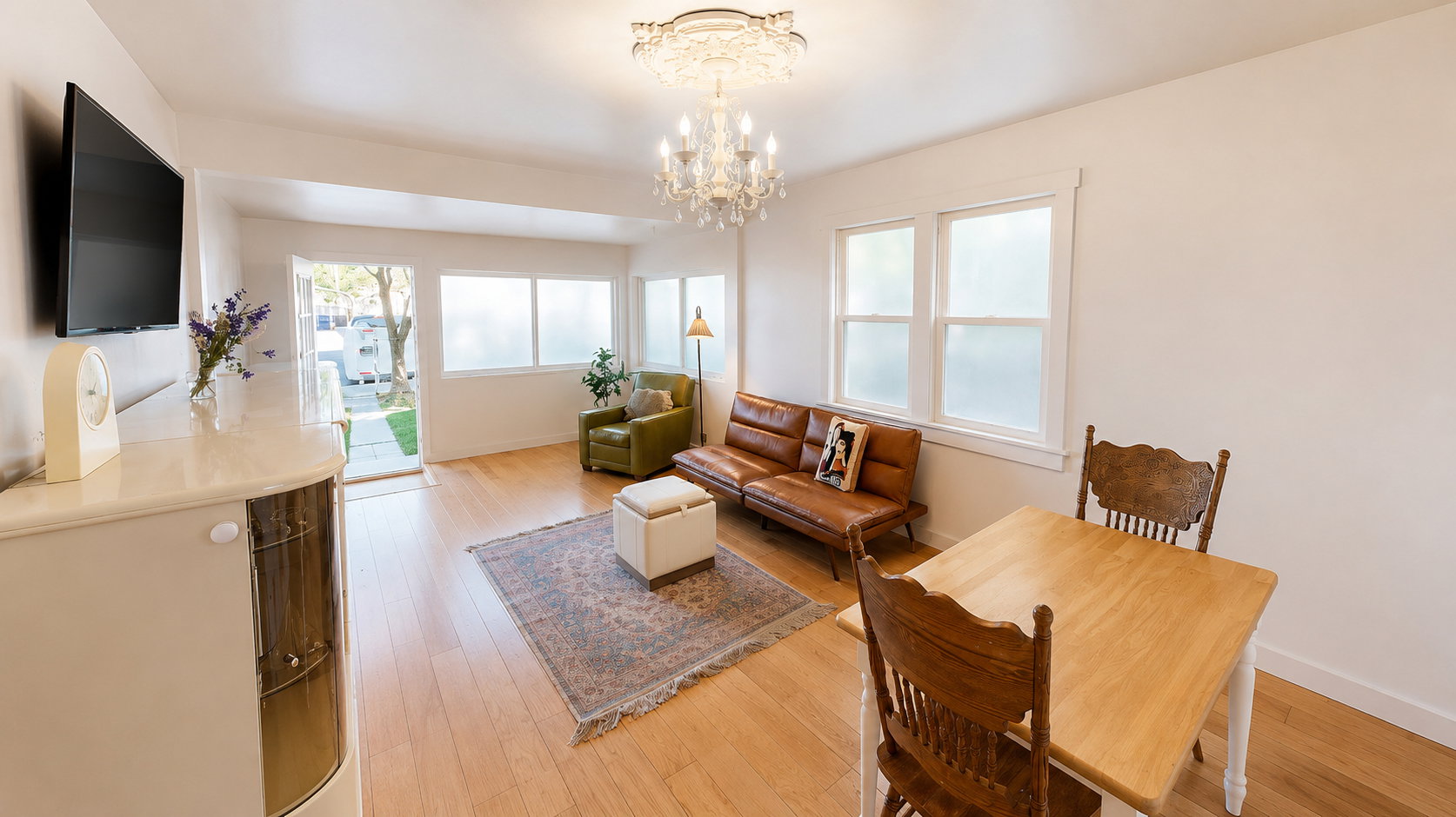 Open-concept living area featuring blonde wood-finish flooring, a decorative chandelier, white walls, and multiple windows with frosted lower panes