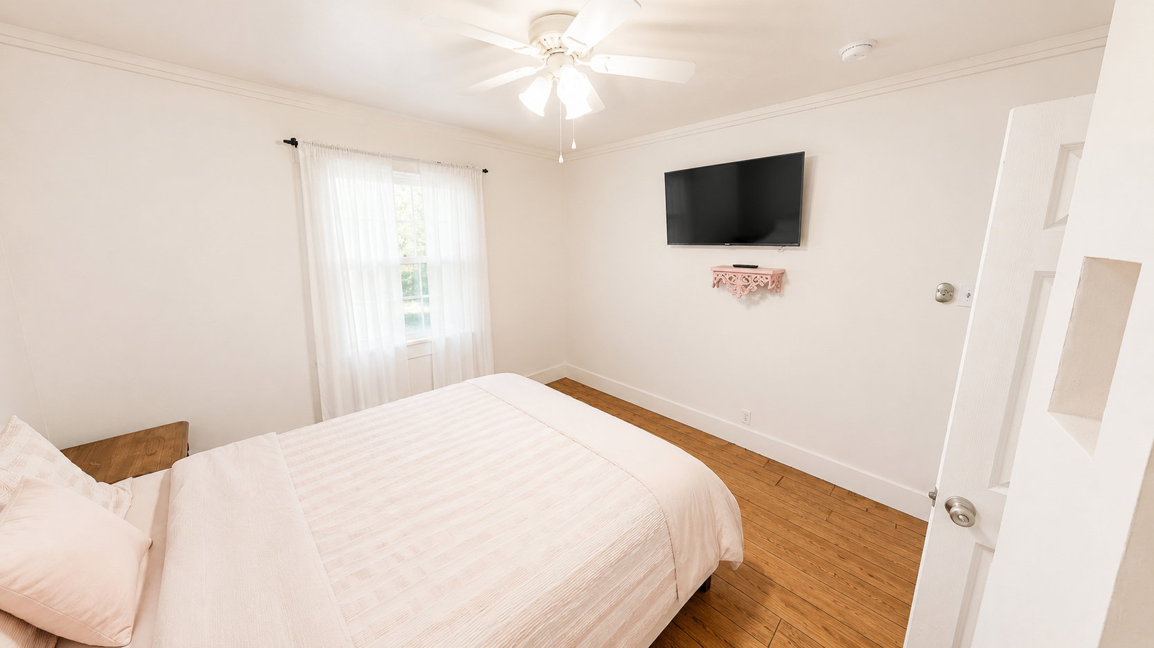 Room featuring wood-finish flooring, a ceiling fan, a window with sheer white curtains, and white baseboards