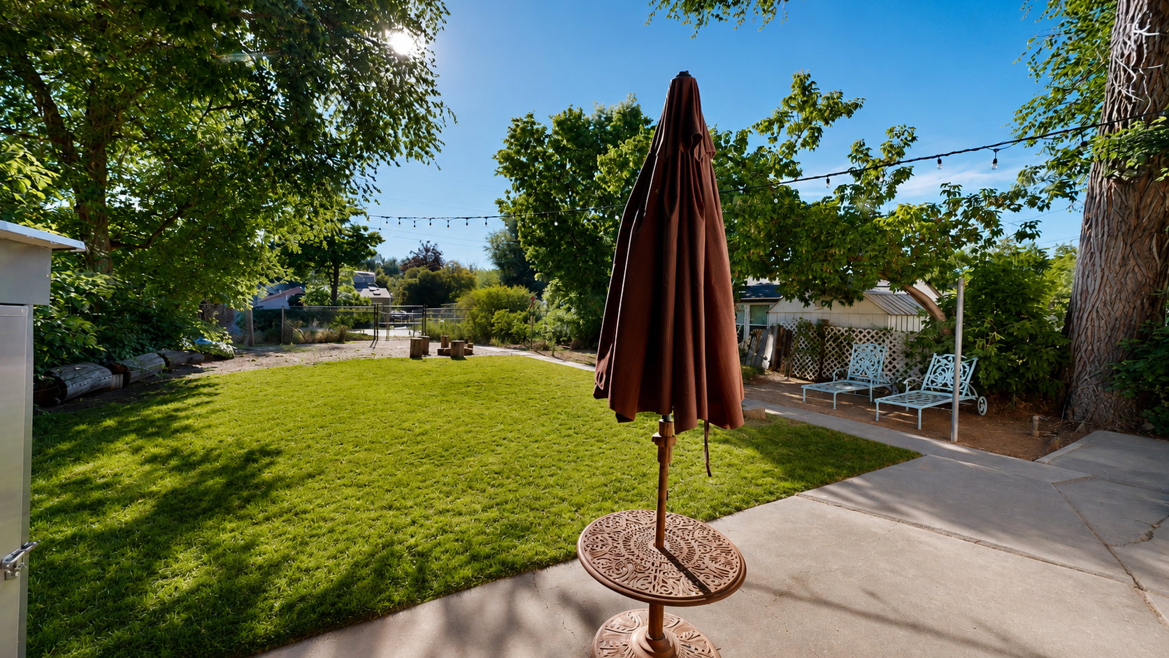 Expansive outdoor area featuring a manicured lawn, concrete patio, mature trees, and string lighting