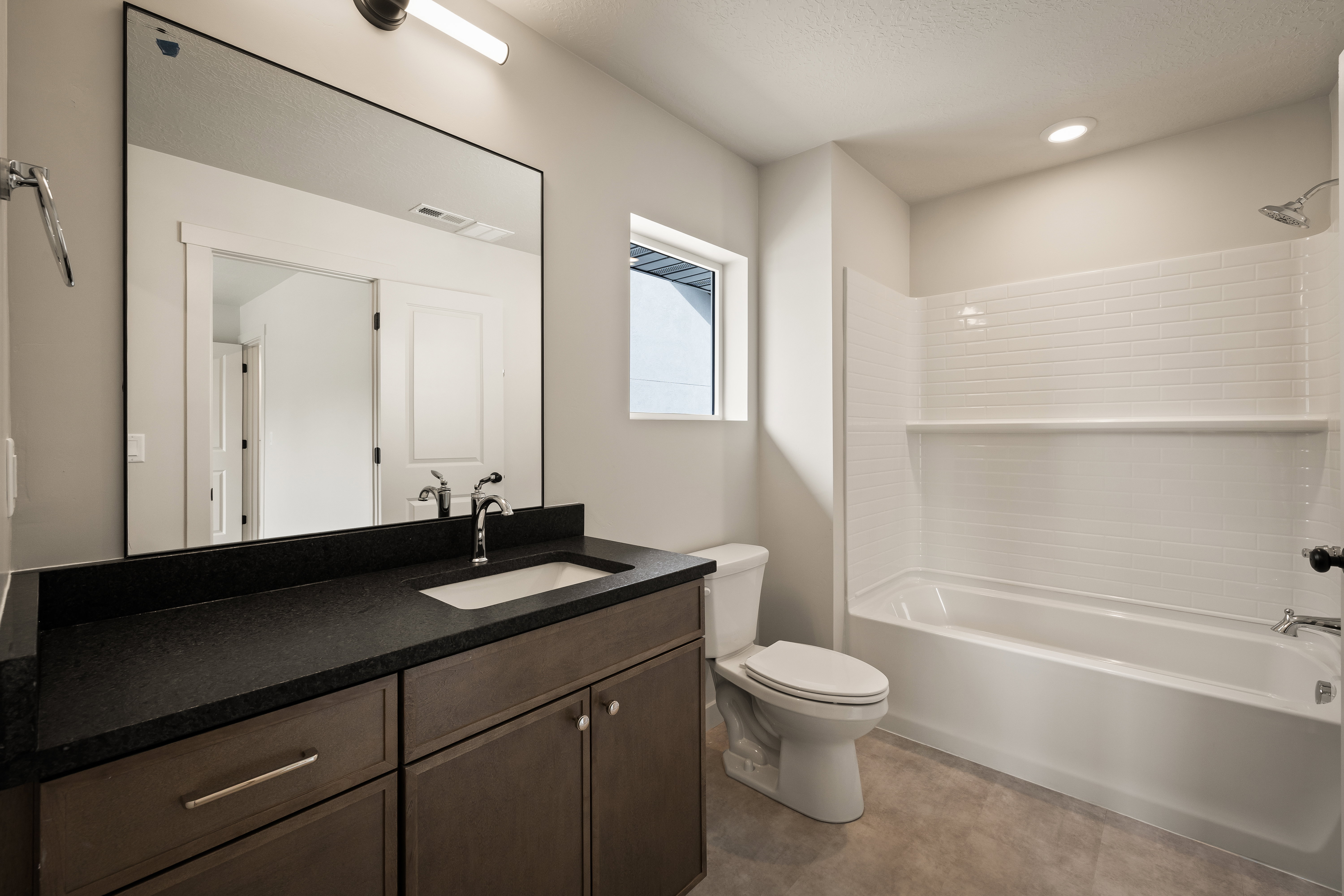 Bathroom featuring a single vanity with a dark countertop and undermount sink, a large framed mirror, a tub/shower combination with subway tile surround, and a window for natural light