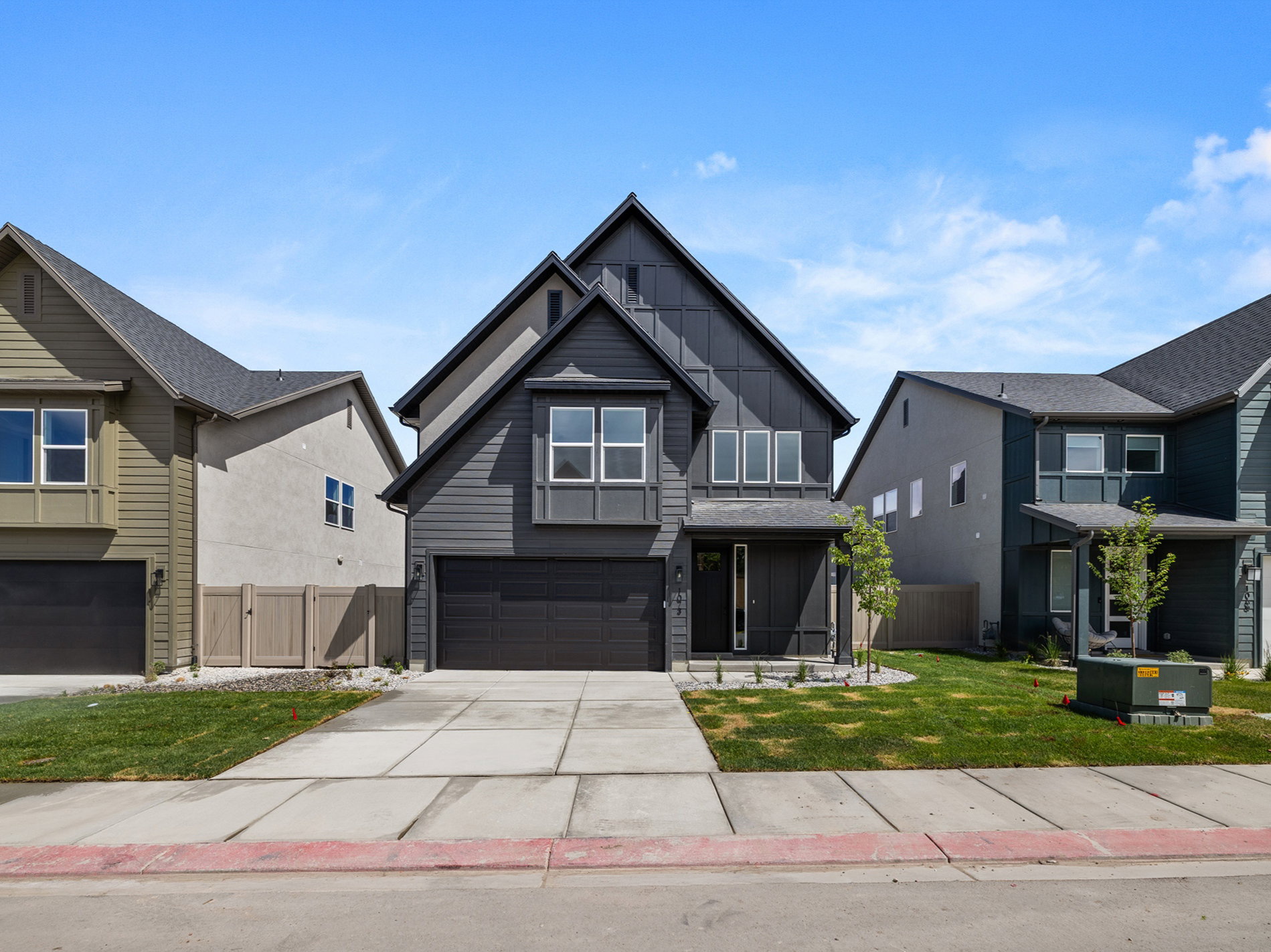 Modern dark gray exterior featuring contrasting siding styles, a prominent front-facing gable, multiple large windows, an integrated two-car garage, and a concrete driveway