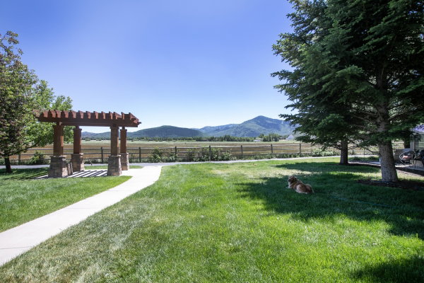 Expansive grassy lawn with a concrete pathway leading to a wood and stone pergola