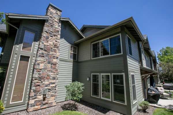 Multi-level exterior featuring horizontal siding in a muted green, a stone-clad chimney, and multiple large windows