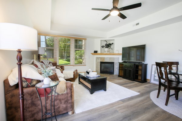 Living area featuring wood-like finish flooring, a ceiling fan, and a fireplace with a stone surround and wood mantel