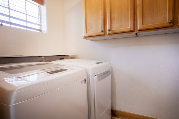 Laundry area with wood-finish upper cabinetry, a window with horizontal blinds, and a built-in shelf