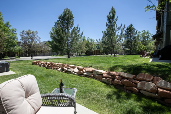Views over expansive green lawn featuring a natural stone retaining wall, mature trees.