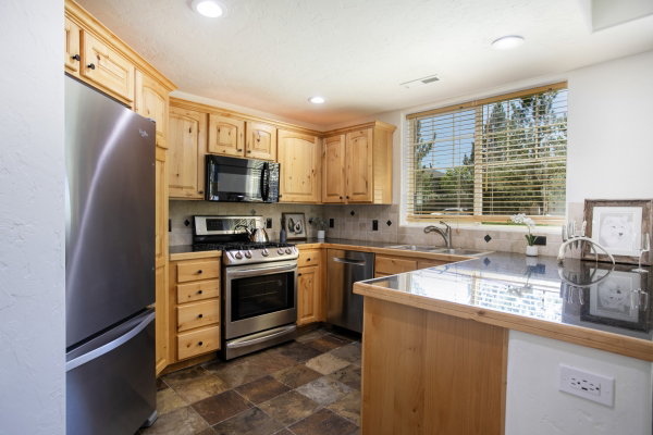 Kitchen featuring light-finish cabinetry, stainless steel appliances, dark granite countertops, and a tile backsplash