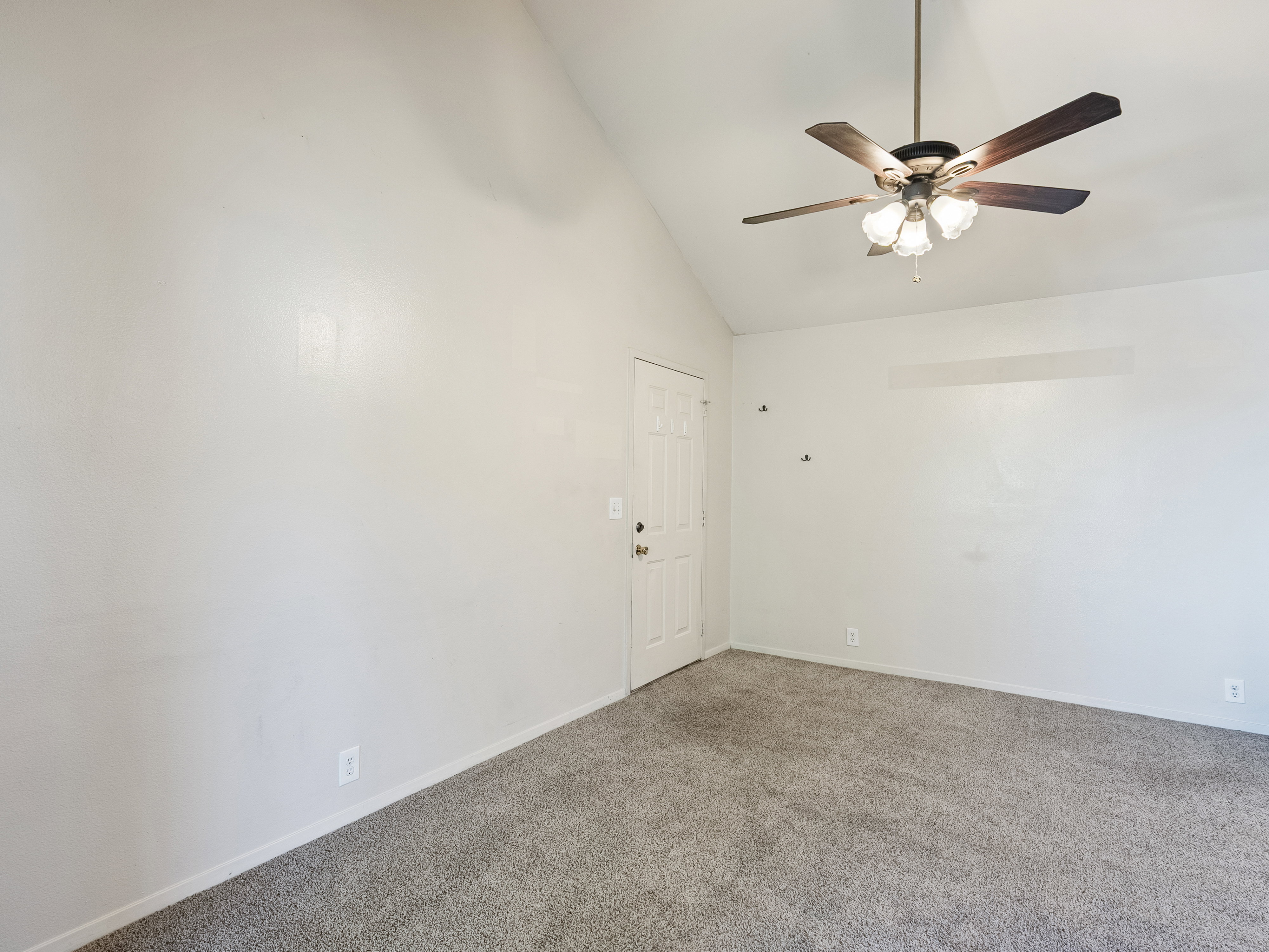 Vaulted ceiling room featuring light gray carpet, a white paneled door, and a multi-blade ceiling fan with integrated lighting