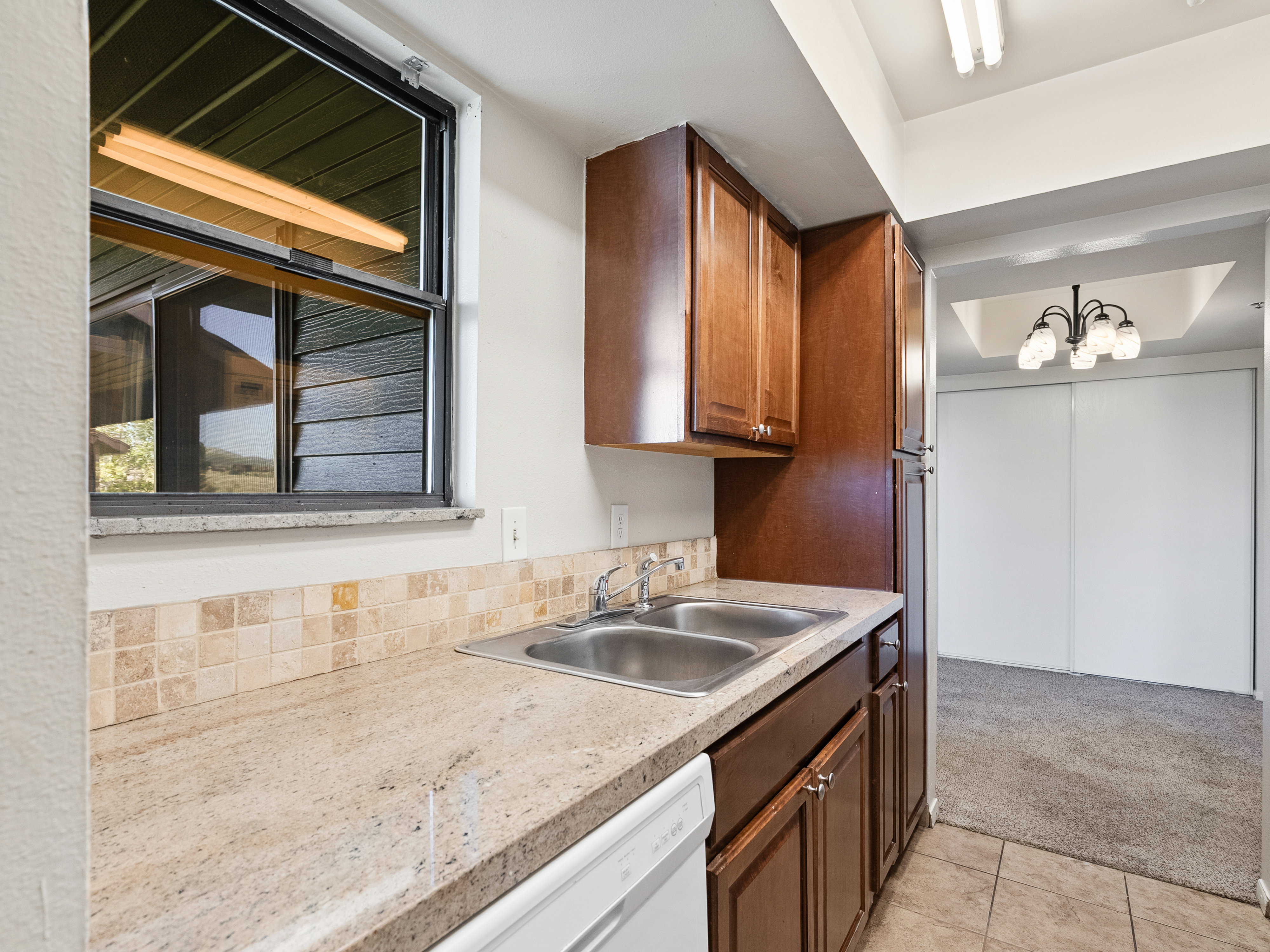 Kitchen featuring wood-finish cabinetry, a dual-basin stainless steel sink, and light-toned countertop