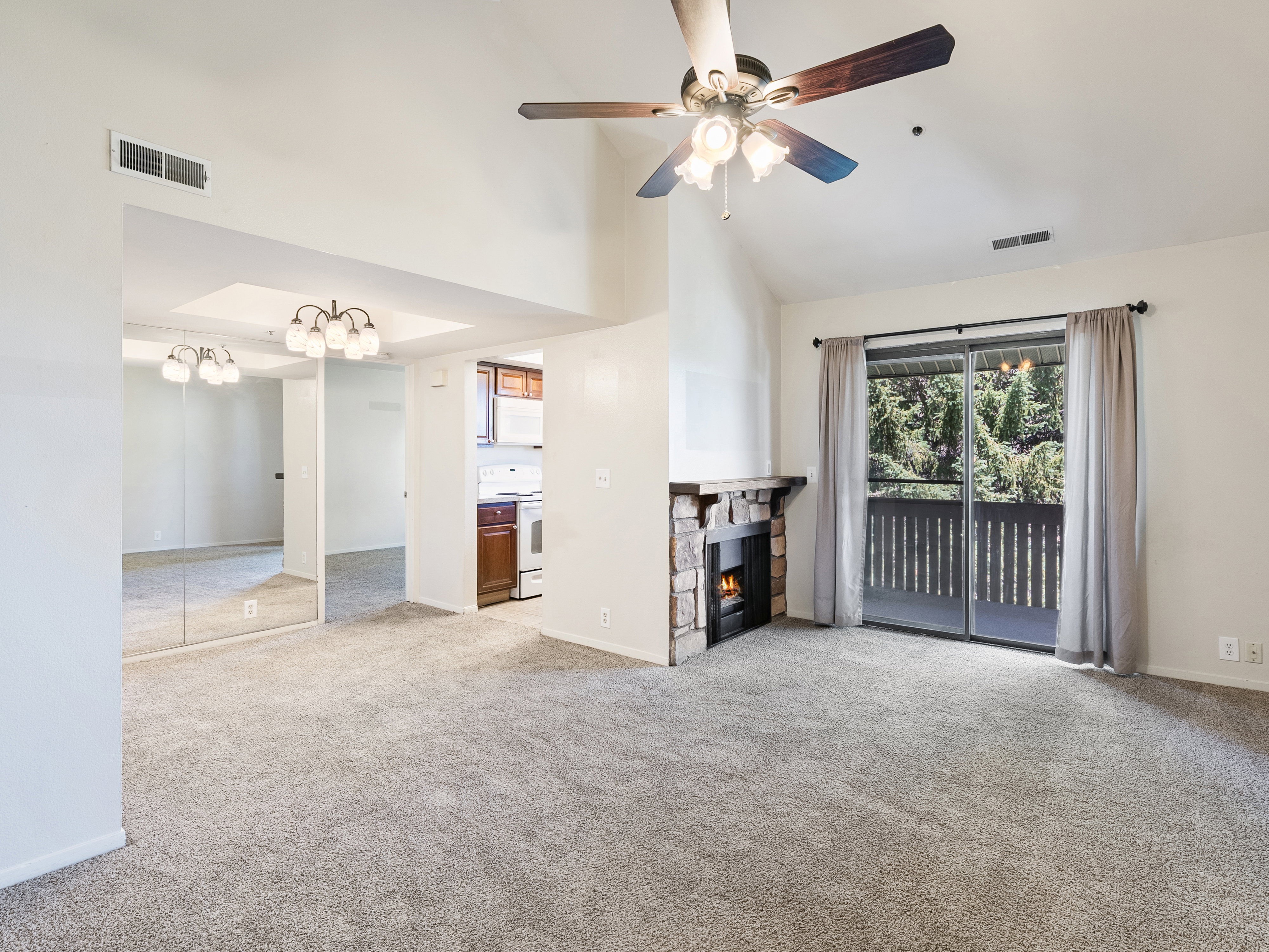 Spacious living area featuring vaulted ceilings, a stone-surround fireplace, and a ceiling fan with integrated lighting