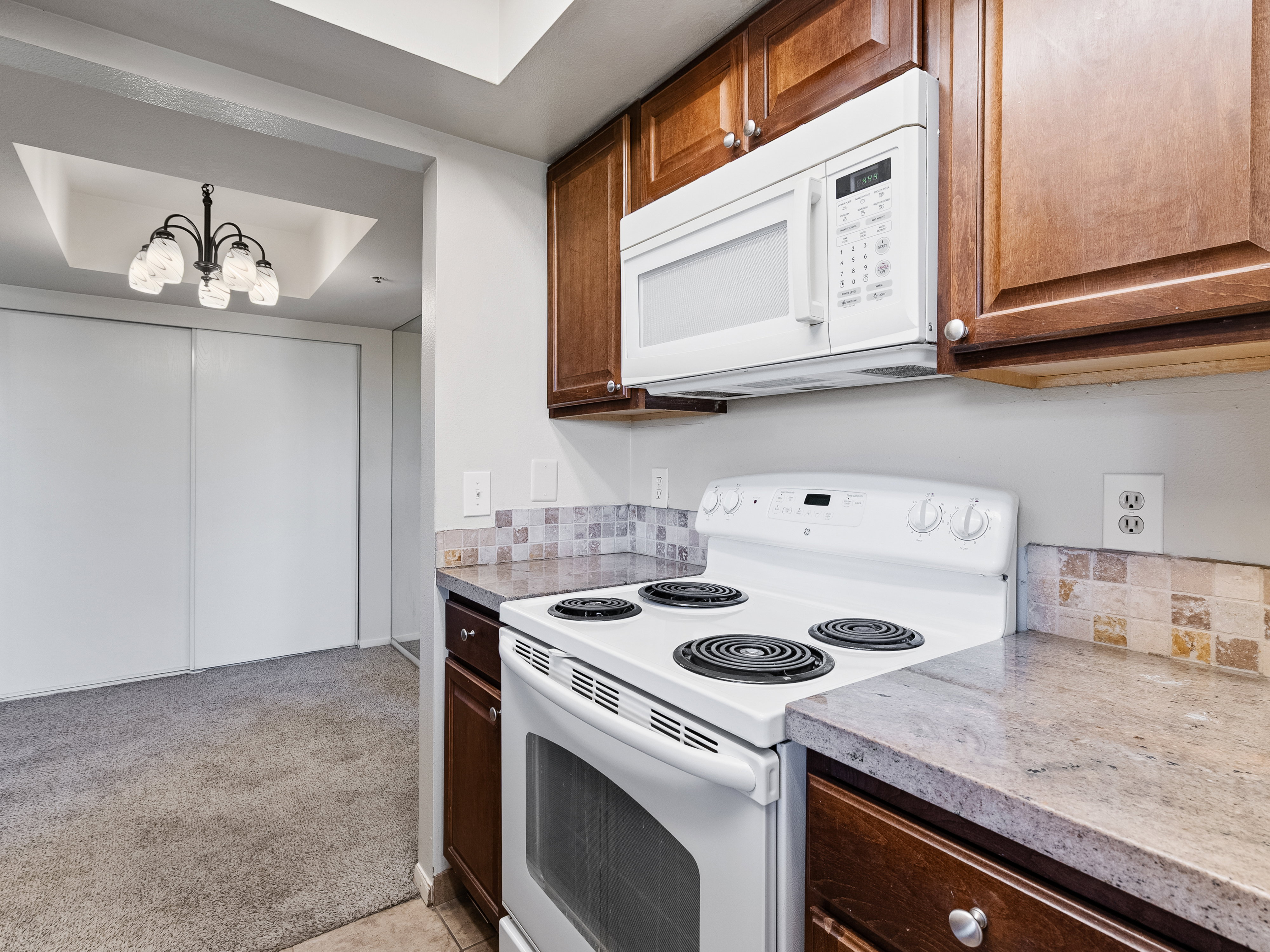 Kitchen featuring white electric range, white built-in microwave, wood cabinetry, stone-look countertops, and tiled backsplash