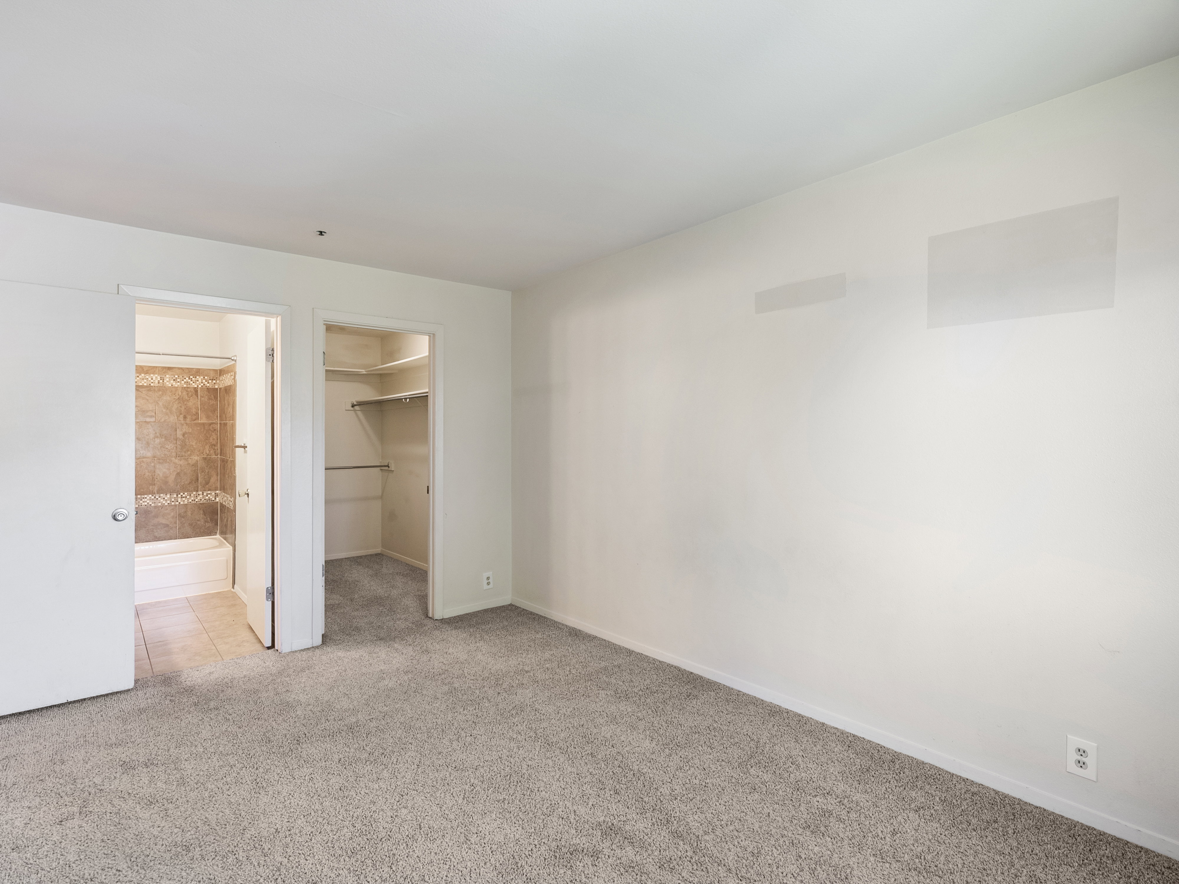 Carpeted interior space featuring a bathroom with a tiled shower-tub combination and an open closet with shelving and hanging rods