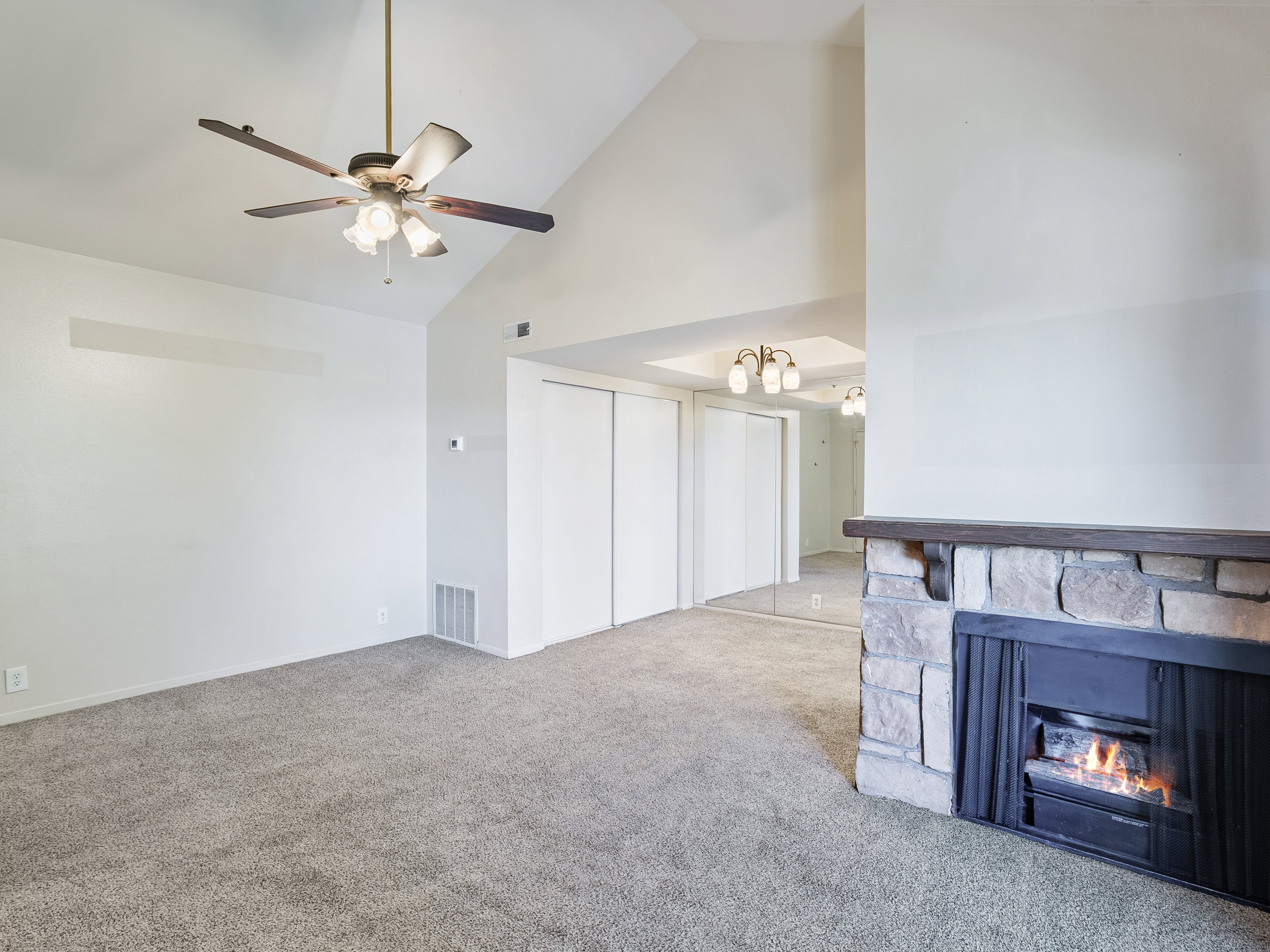 Living area featuring a stone fireplace with a wood-finish mantel, vaulted ceiling with a ceiling fan, and carpet flooring