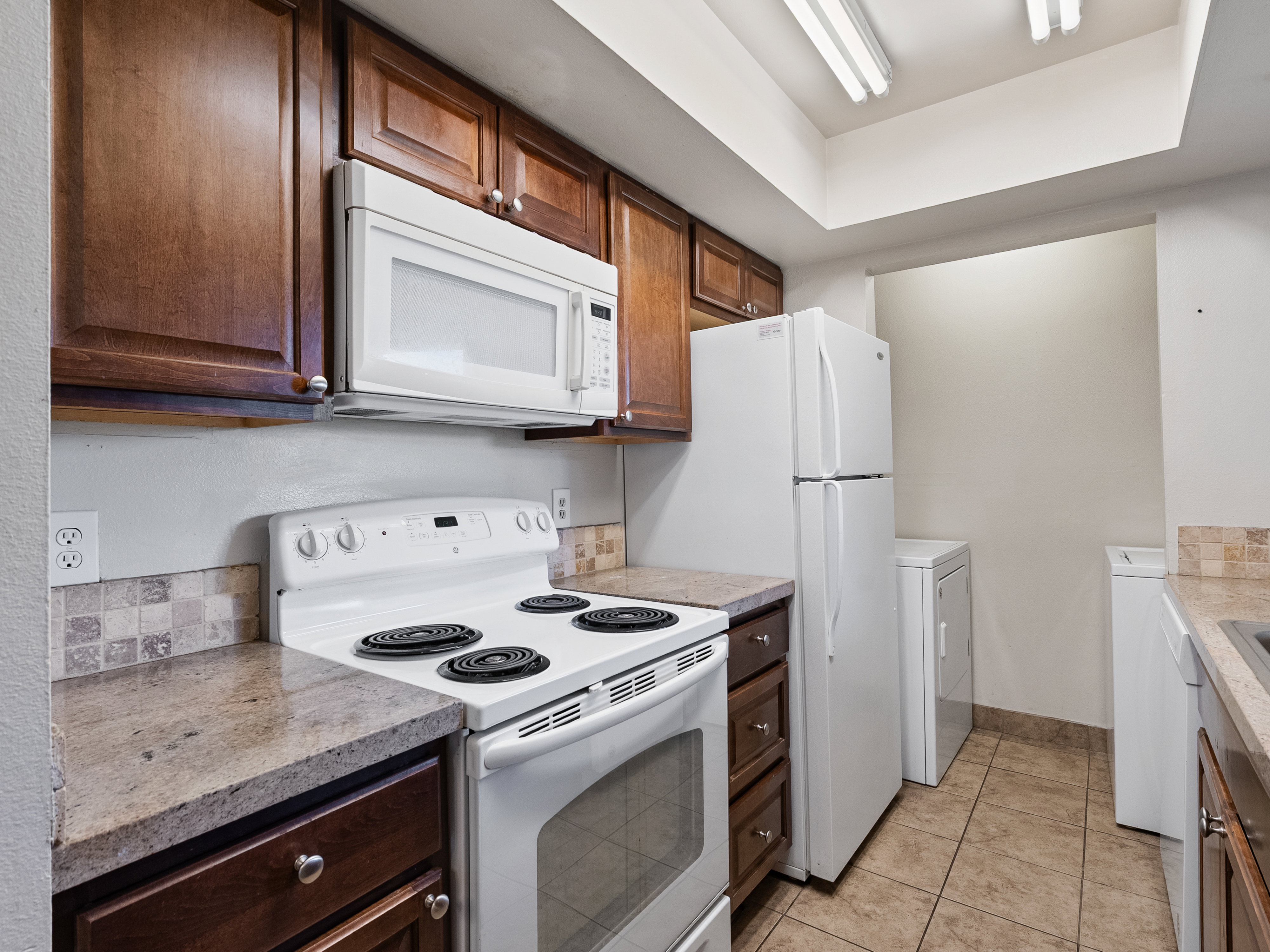 Kitchen featuring wood-finish cabinetry, white appliances, and a tiled backsplash