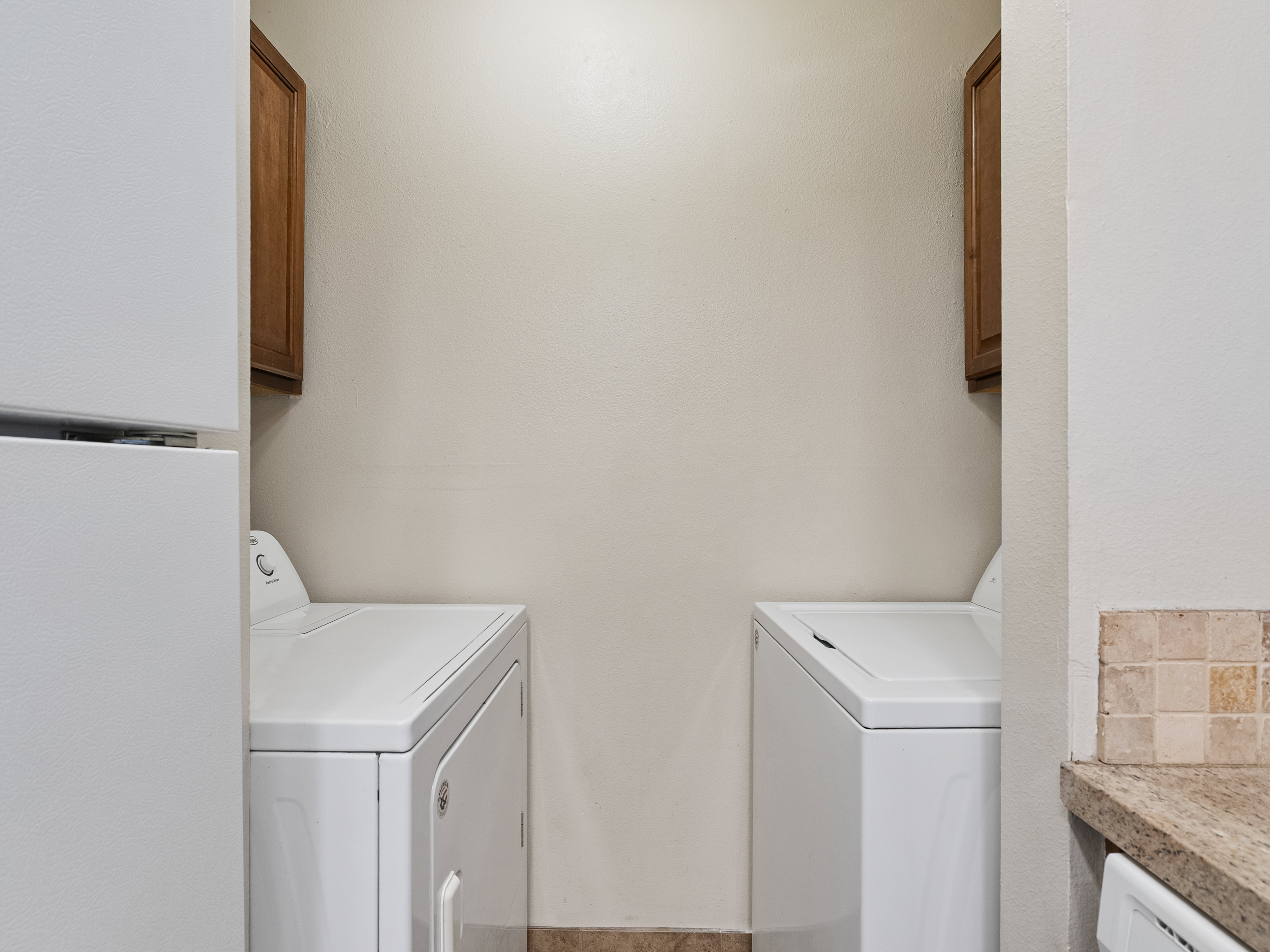 Dedicated laundry area featuring a washer and dryer, upper cabinetry, and tile flooring