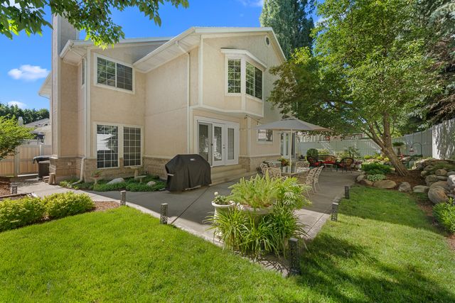 Spacious rear patio featuring a stucco exterior with stone accents, multiple large windows, and a mature tree providing natural shade