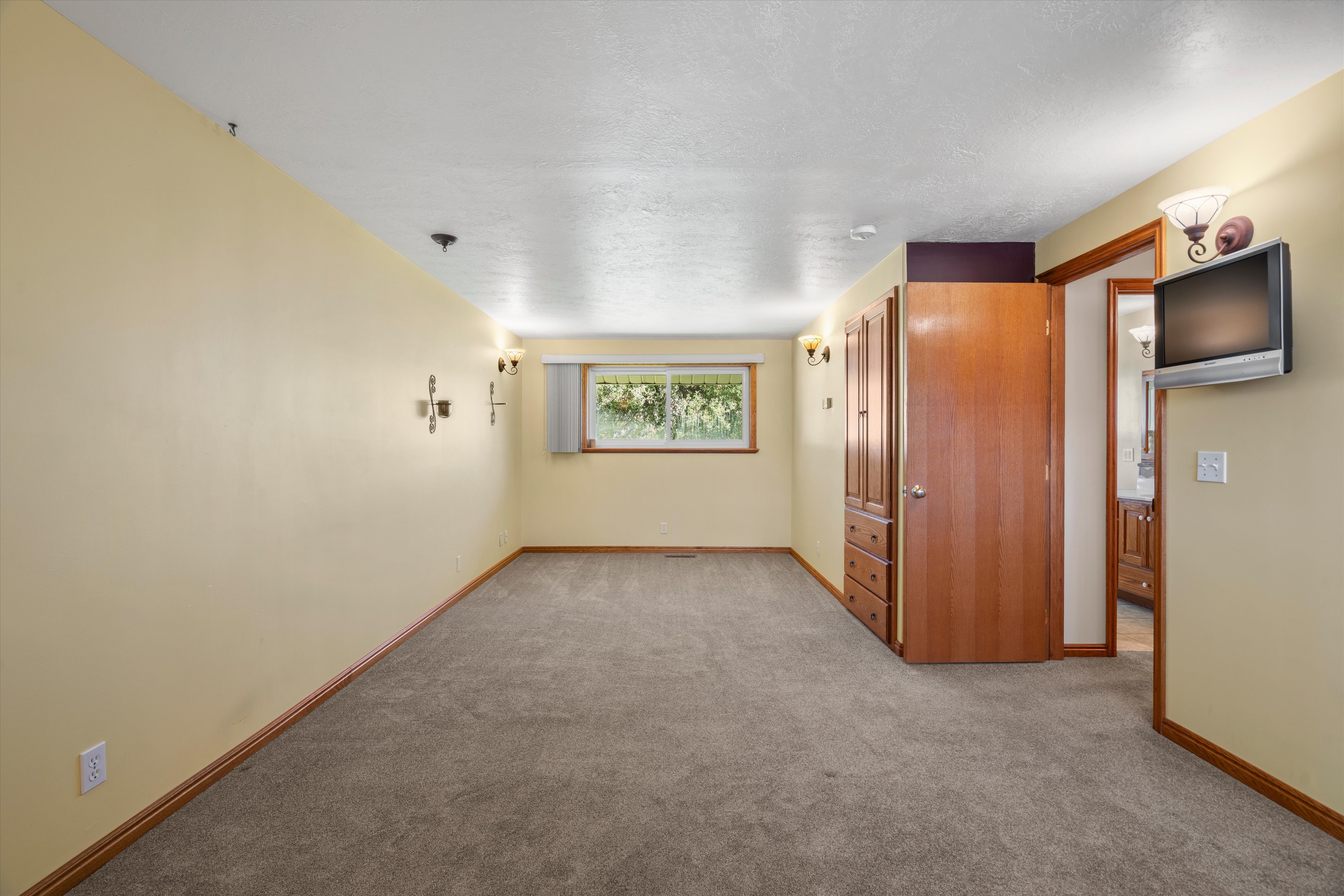 Spacious interior room featuring light-toned carpeting, a window with natural light, and built-in wood cabinetry with drawers
