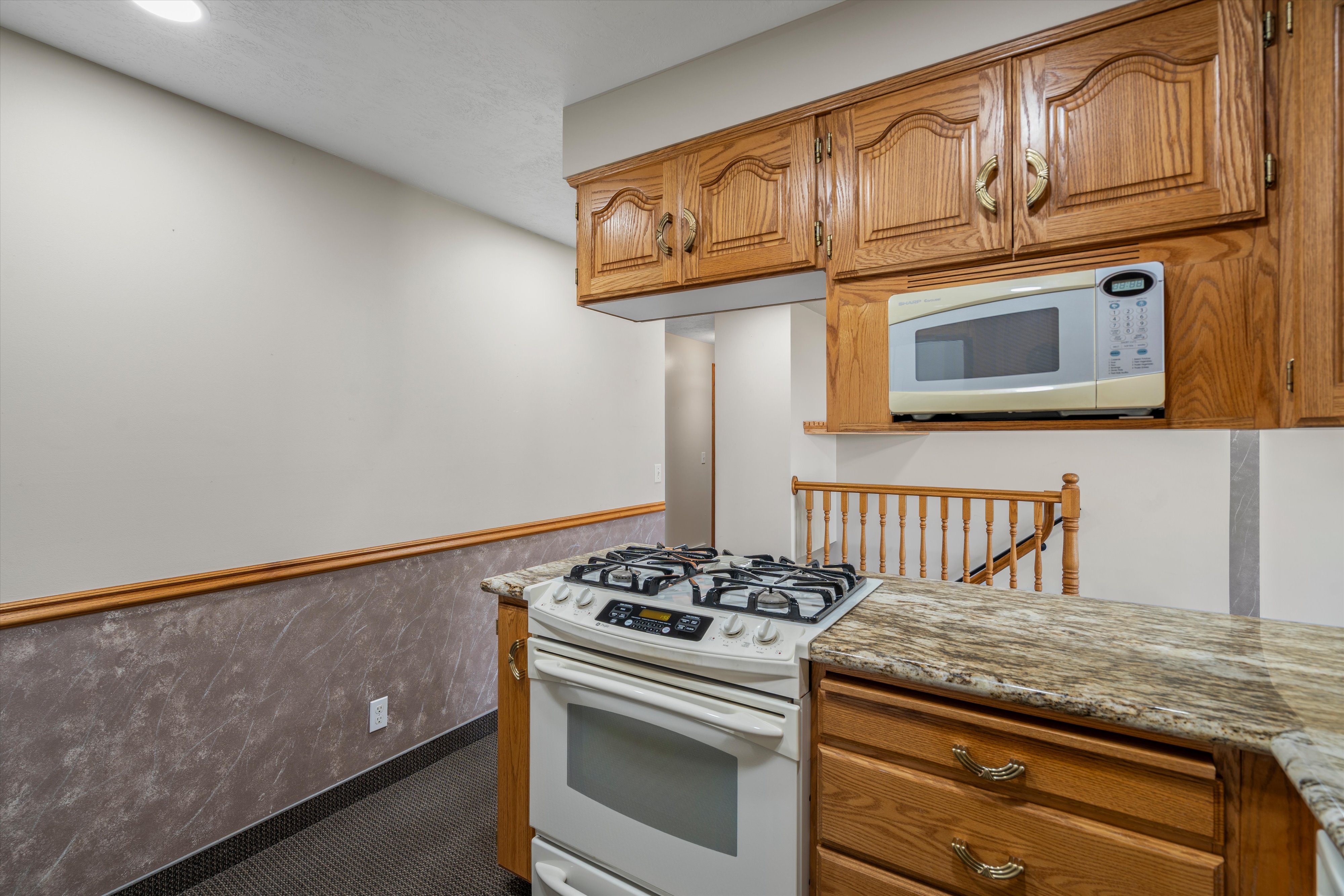 Kitchen featuring wood cabinetry, light-toned countertops, a built-in microwave, and a gas range