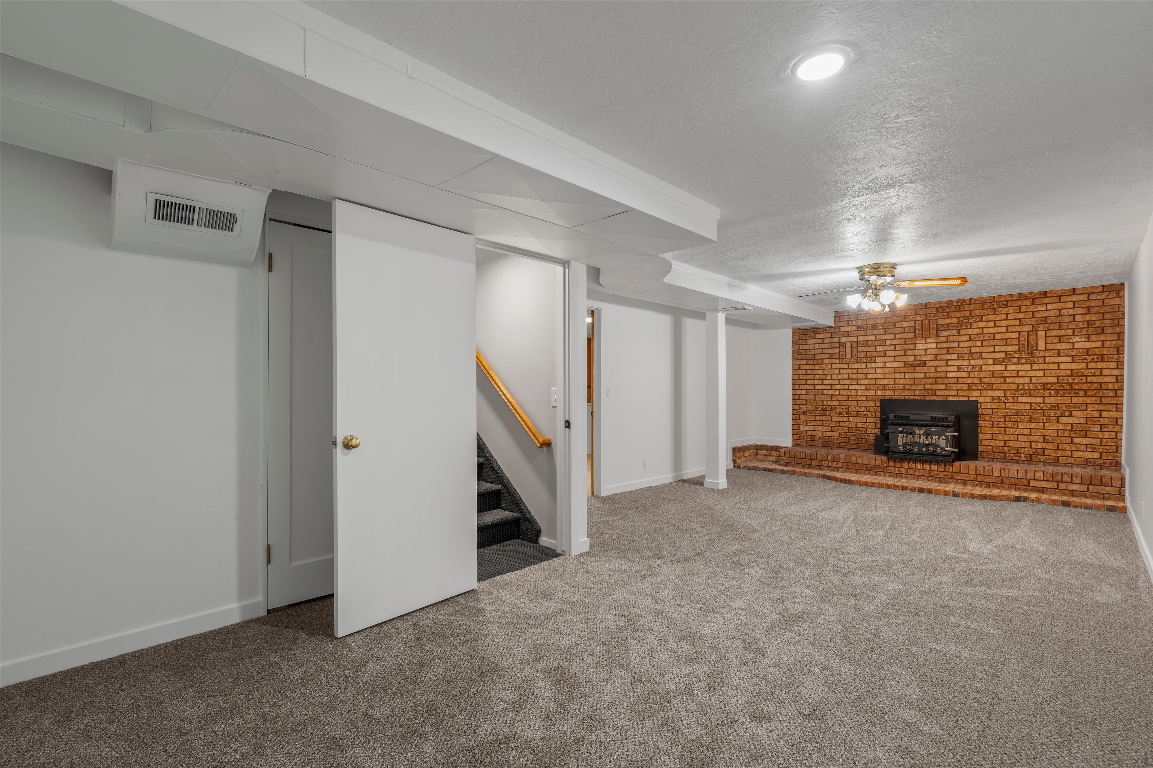 Spacious room featuring a brick fireplace with a raised hearth, light gray carpet, recessed lighting, and a ceiling fan