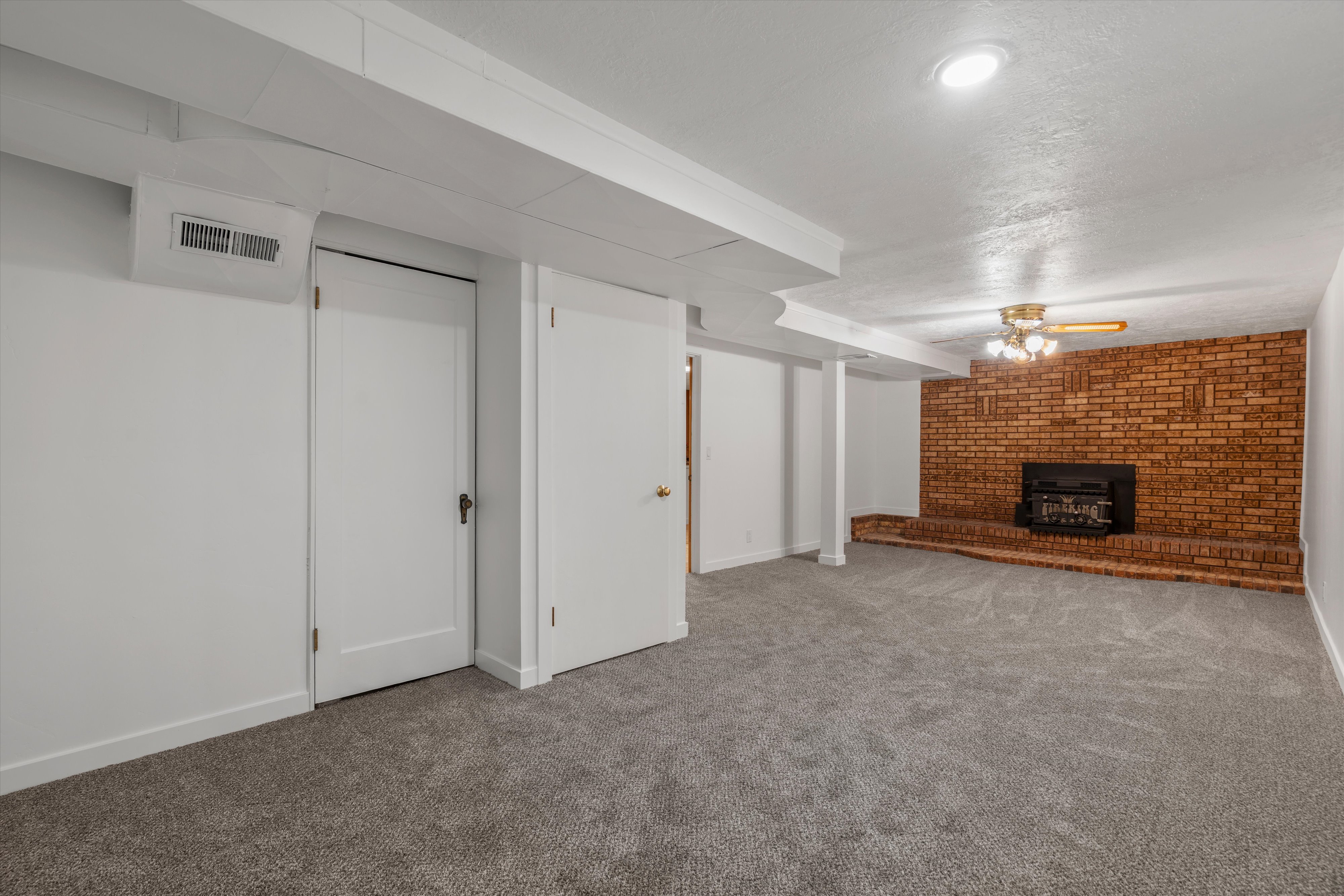 Spacious room featuring a brick-surround fireplace with hearth, recessed lighting, and a ceiling fan