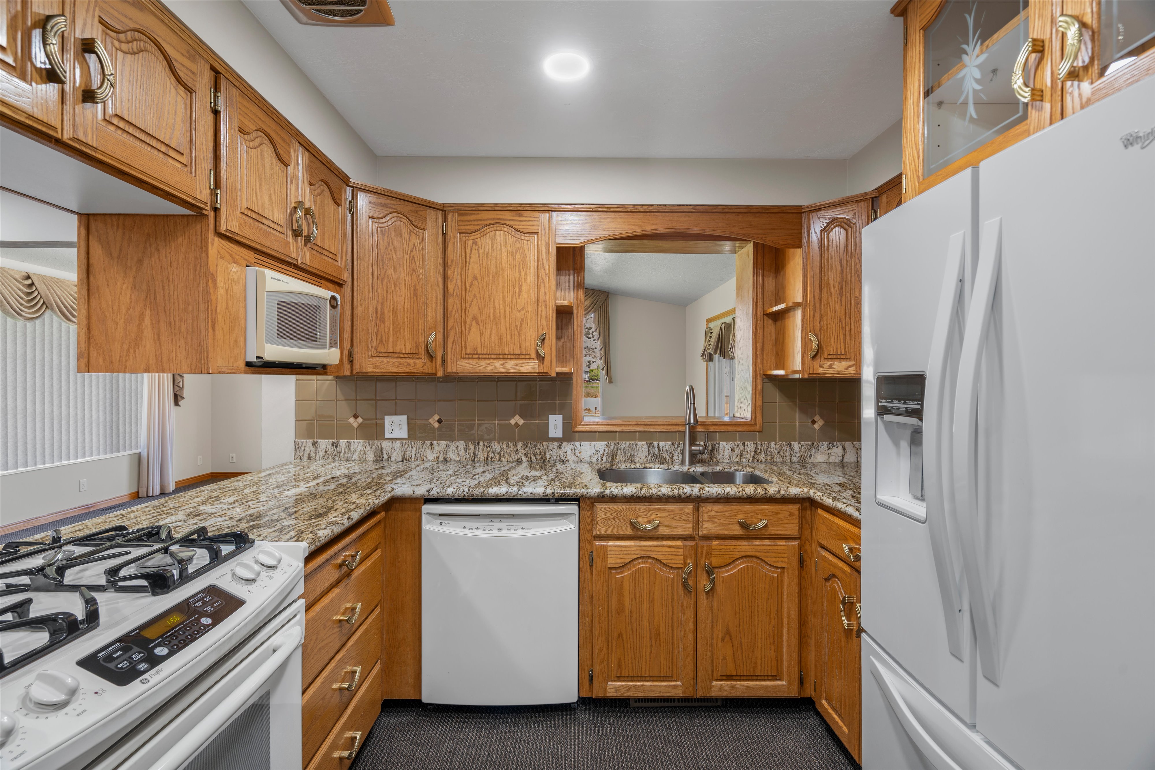 Kitchen featuring wood cabinetry, stone countertops, a tile backsplash, and a pass-through window