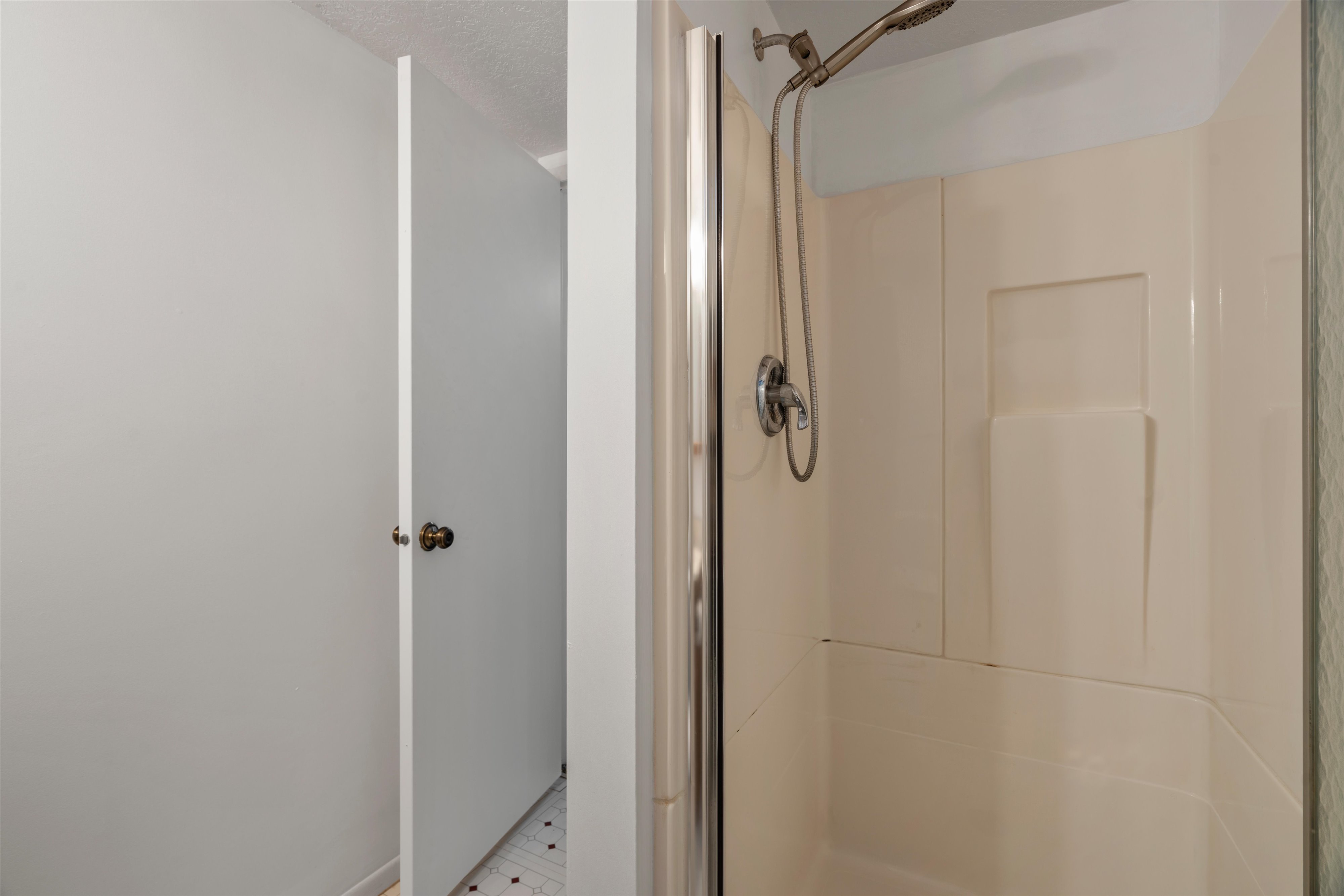 Shower enclosure featuring a chrome shower head and handle, with an adjacent doorway