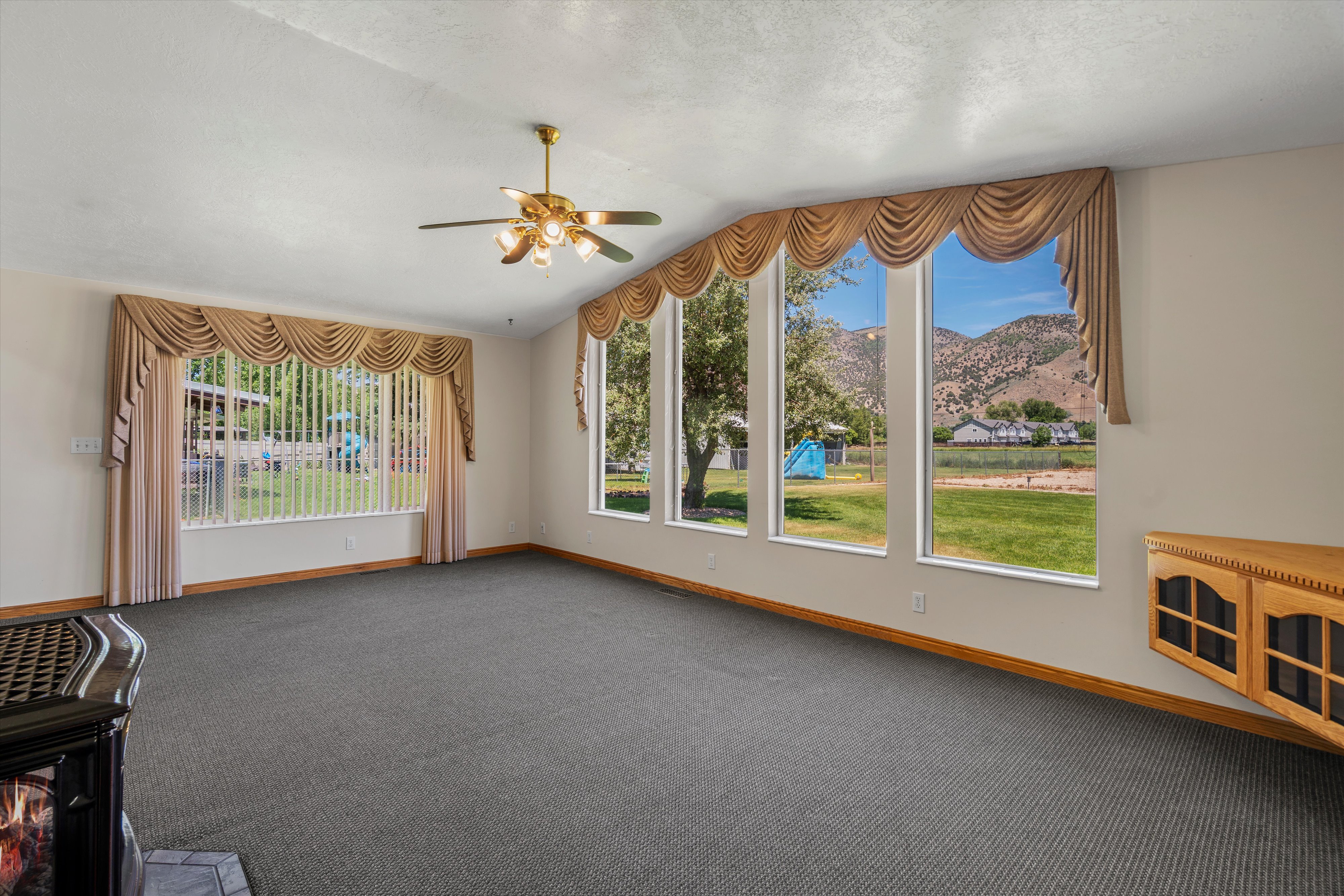 Expansive living area with large windows, wall-to-wall carpeting, and a ceiling fan with integrated lighting