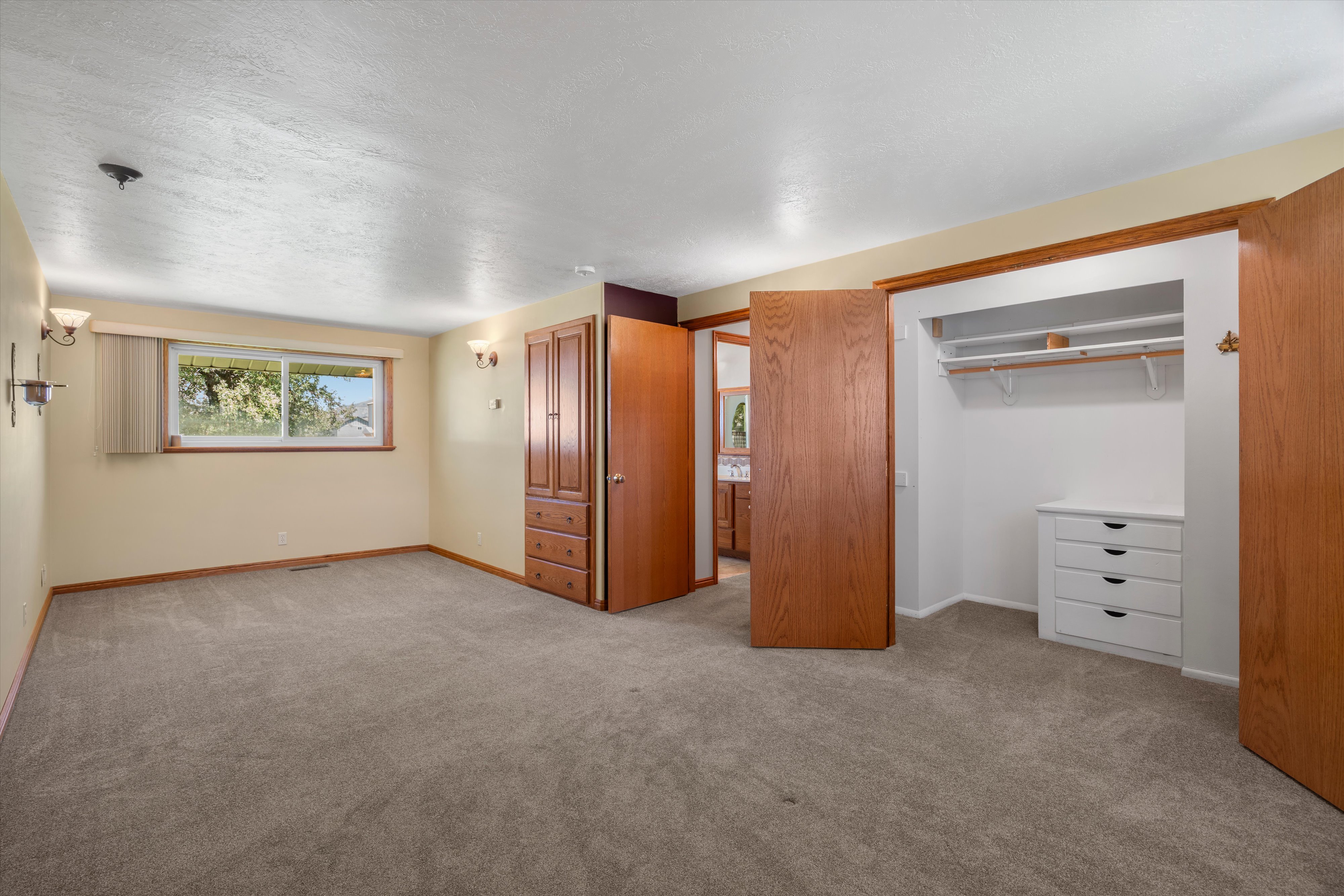 Spacious carpeted room featuring a window with exterior visibility, wood-trim baseboards, and two wall sconces