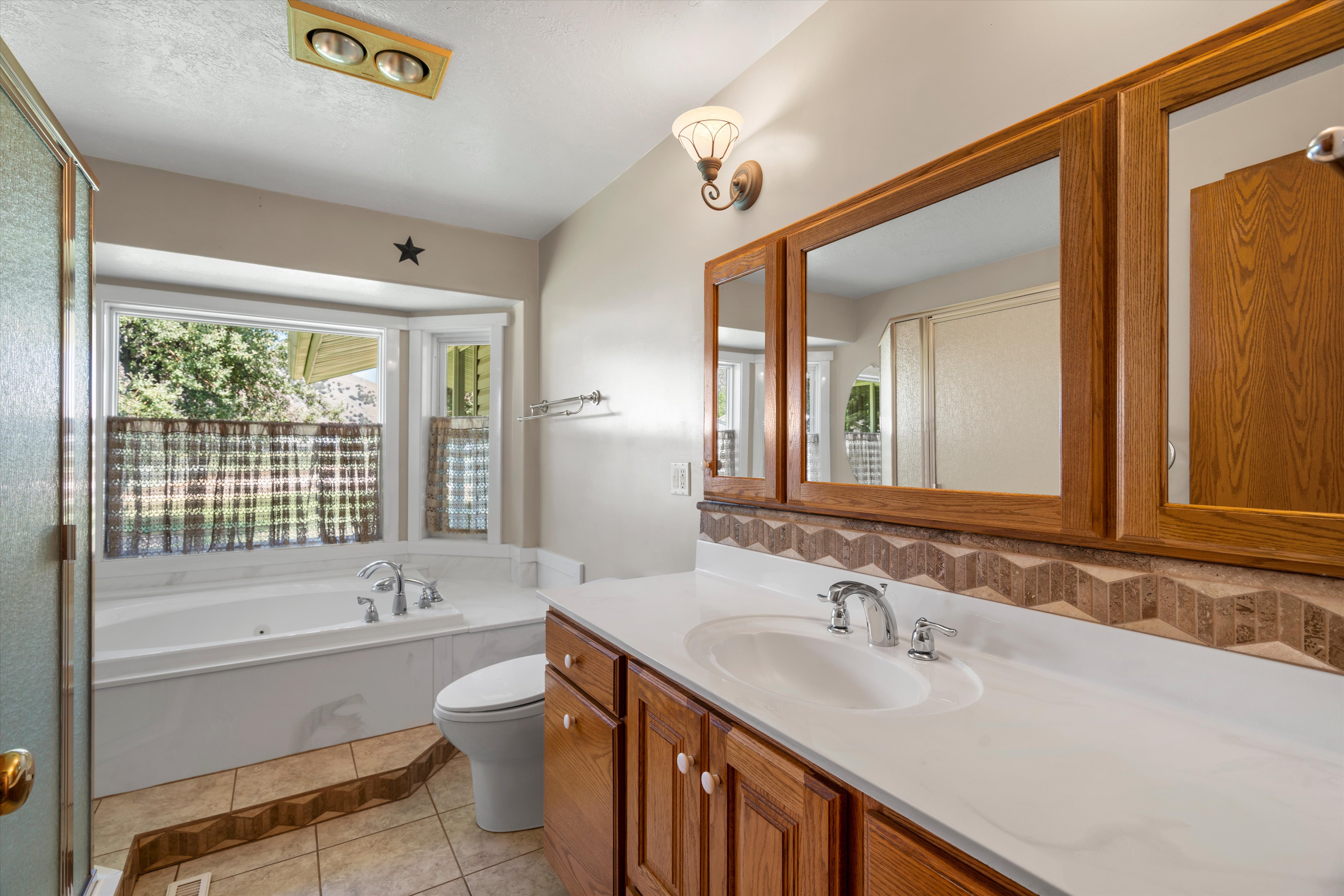 Bathroom featuring a bay window, built-in soaking tub, vanity with dual sinks, overhead lighting, and tile flooring