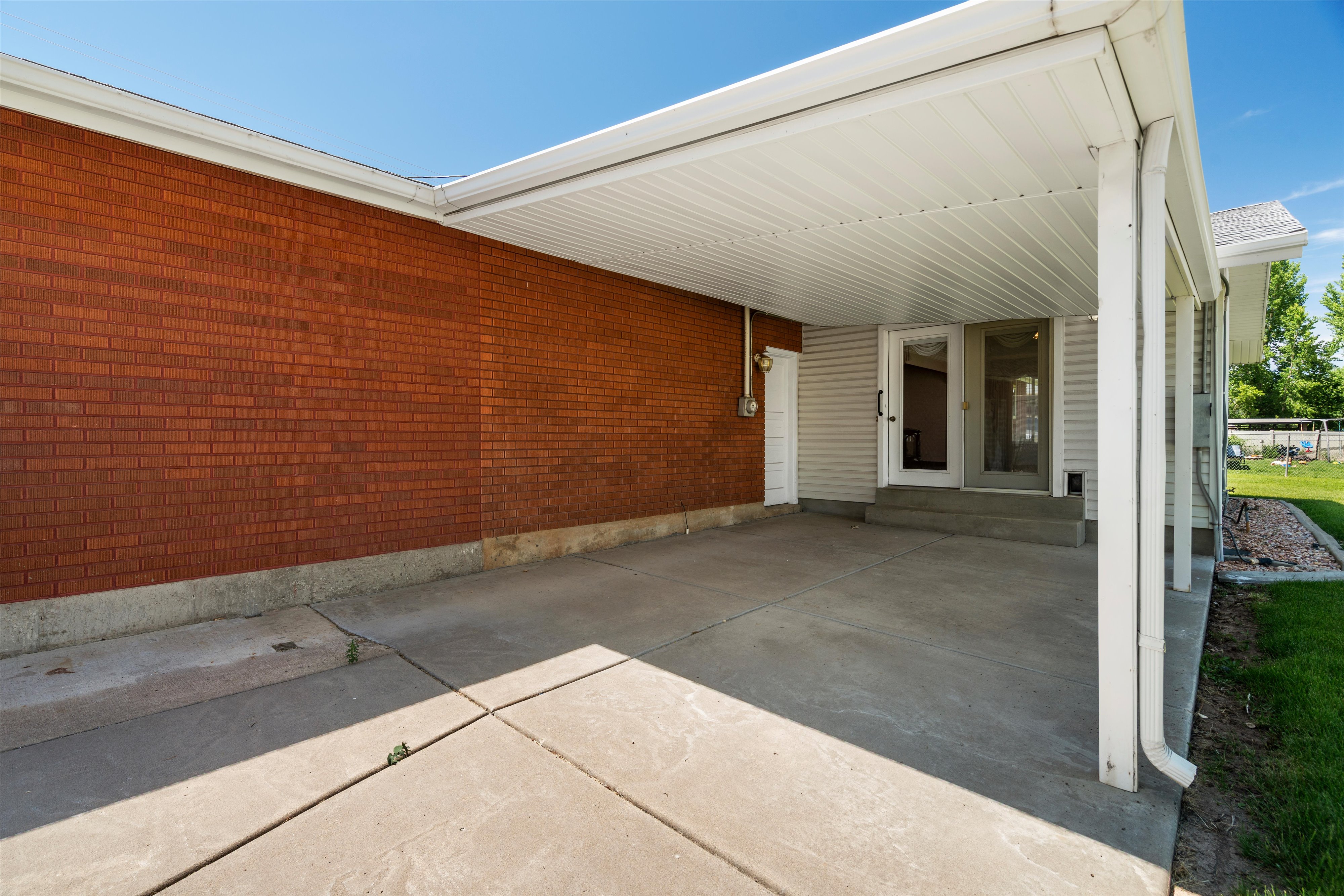 Covered patio area with concrete flooring, brick exterior, and white siding