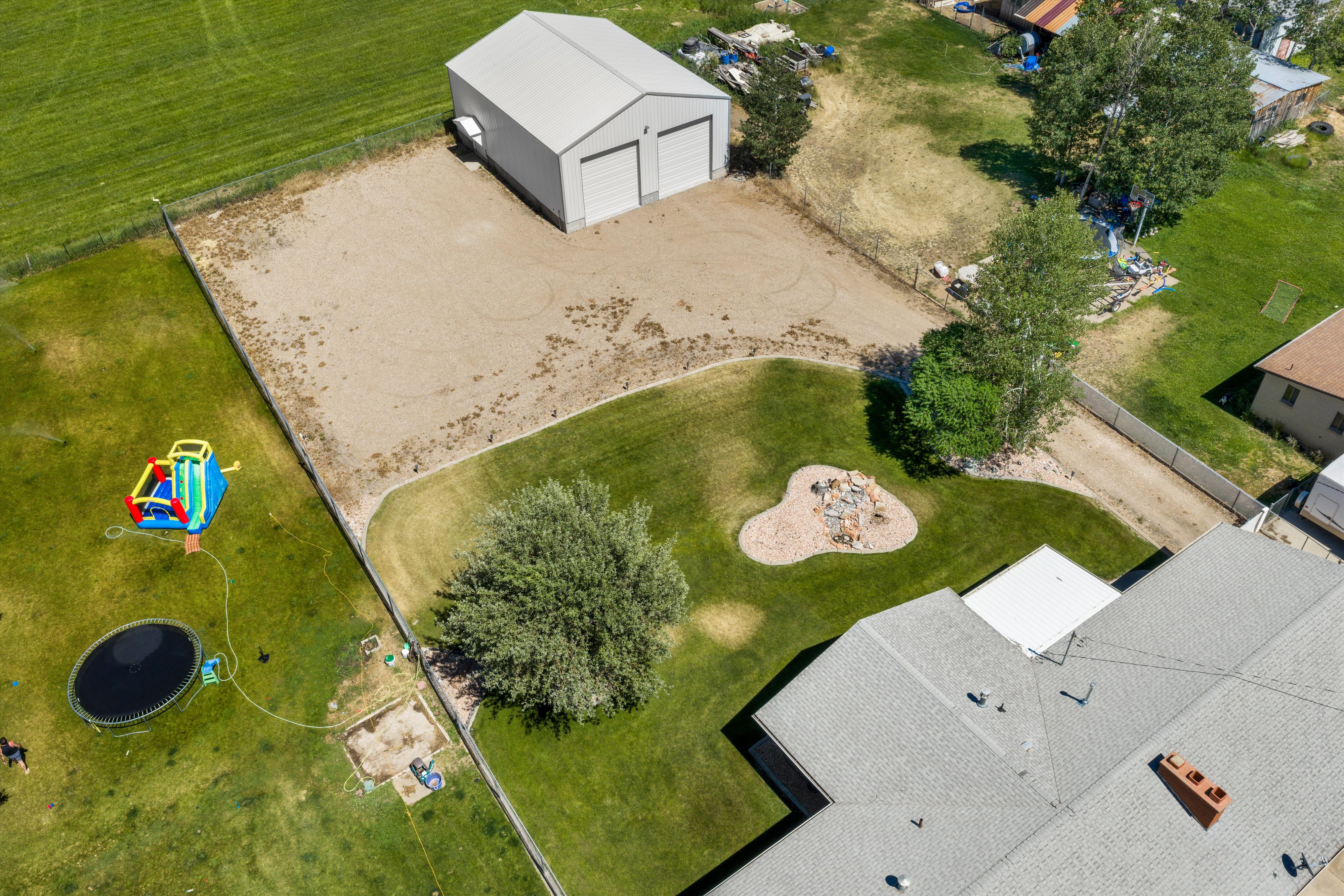 Expansive property featuring a two-car metal outbuilding, a circular gravel fire pit area, and a large grassy lawn