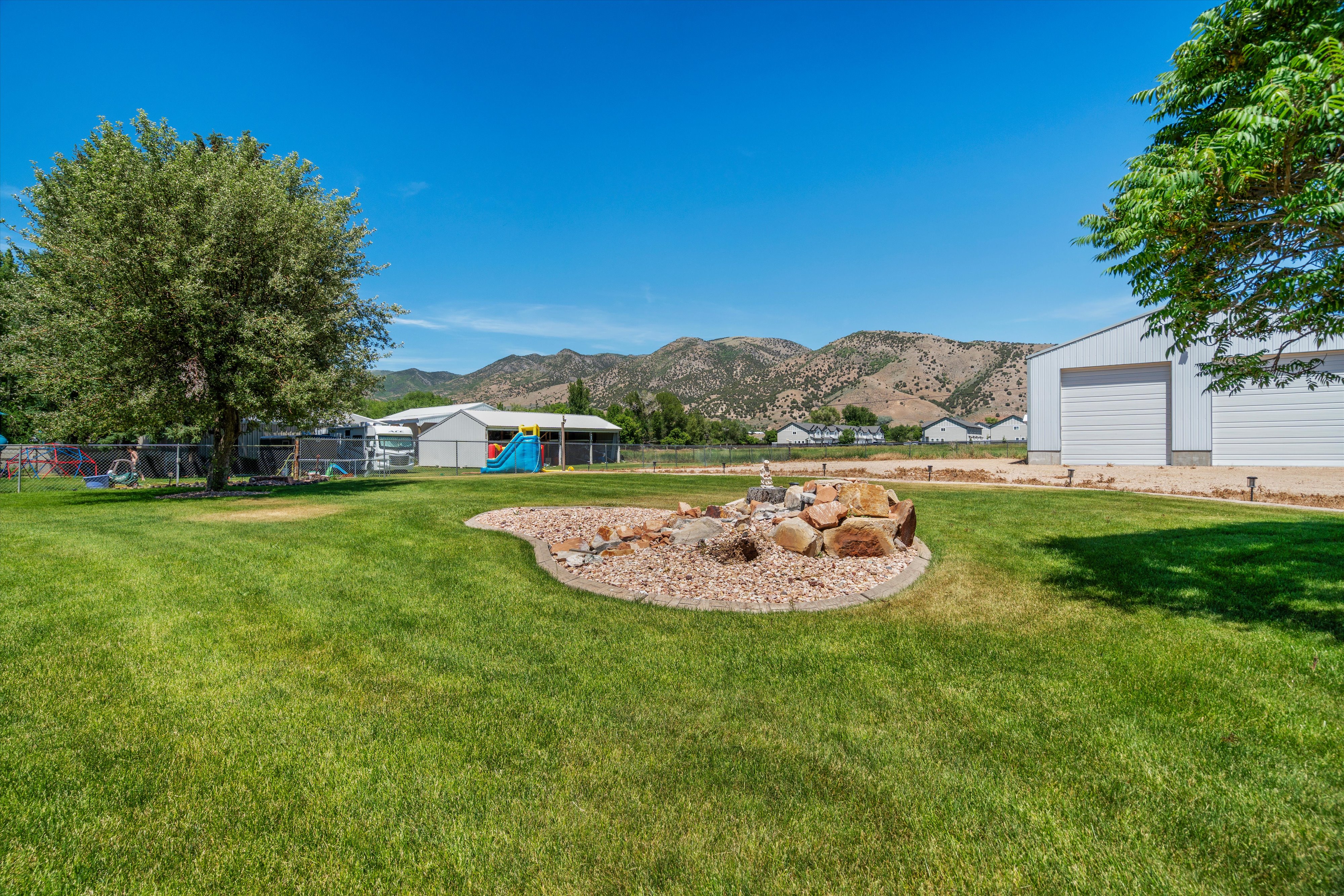 Expansive green lawn with a rock-bordered landscape feature, mature tree, and distant mountain backdrop