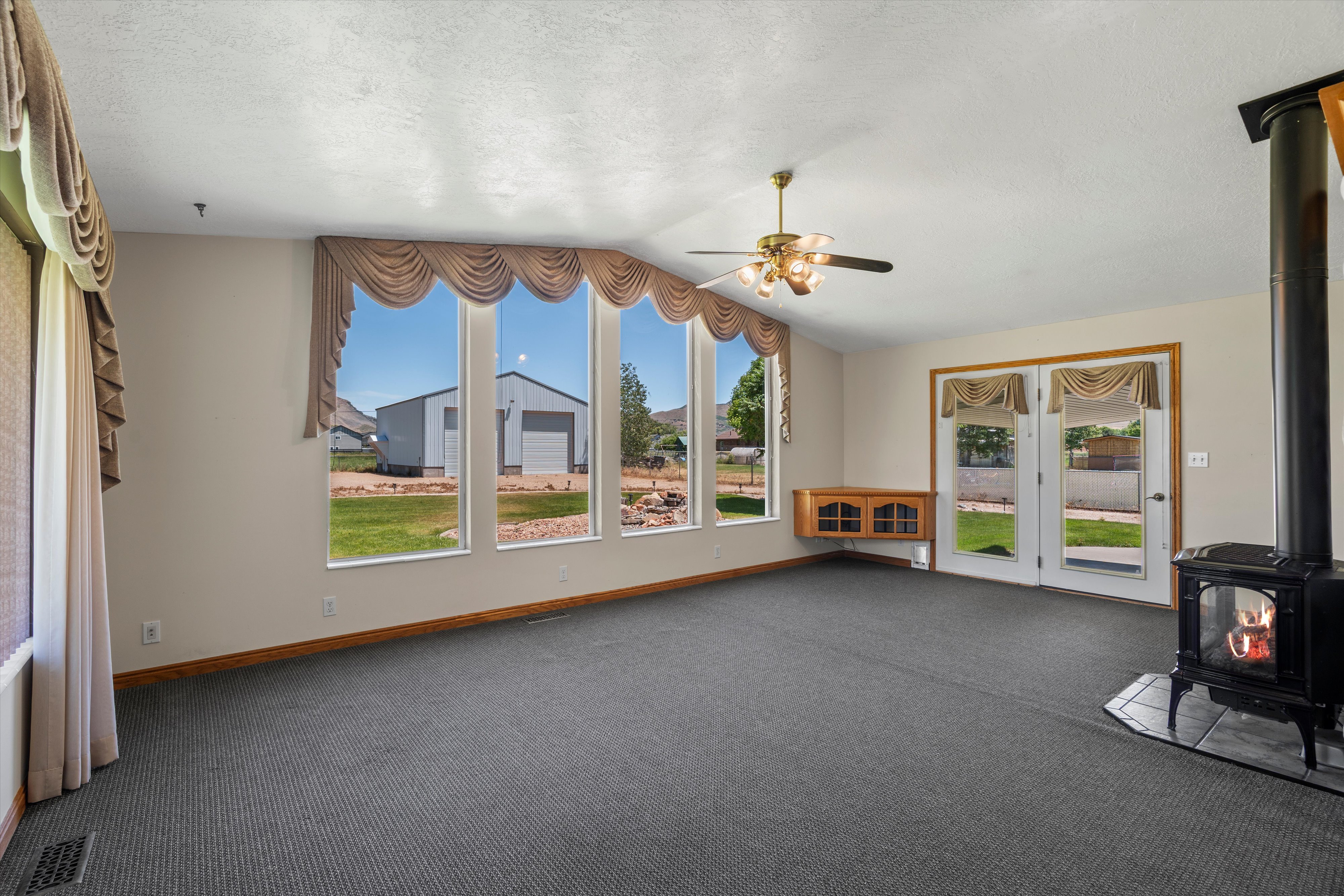 Interior living space featuring expansive windows, a ceiling fan, wood-finish flooring, a built-in wood-finish cabinet, and a black wood-burning stove with a tile hearth
