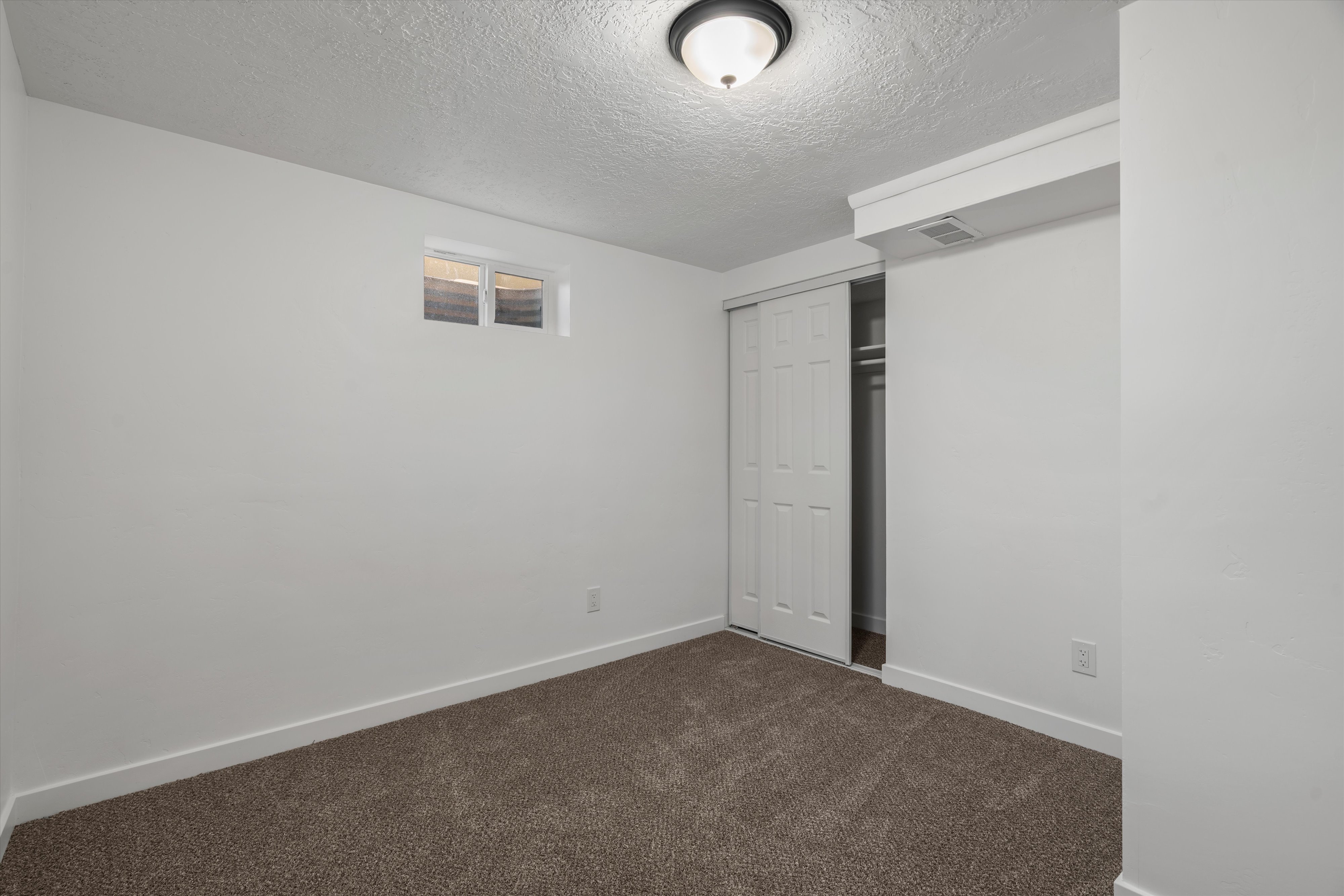 Spacious room featuring neutral carpeting, white baseboards, a single window, and a closet with bi-fold doors