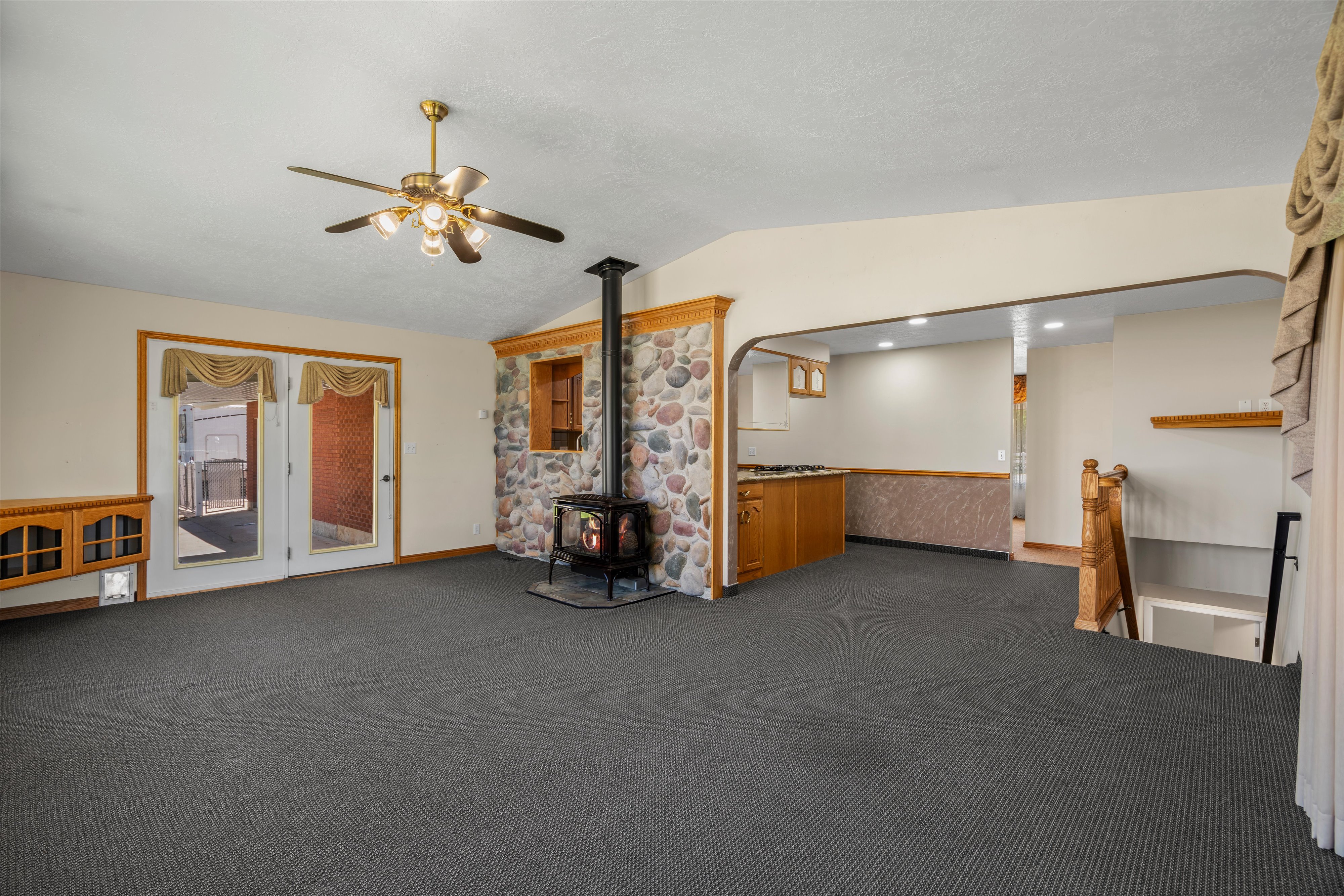 Spacious room featuring a stone-clad wood-burning stove, double glass panel doors, and a ceiling fan with integrated lighting