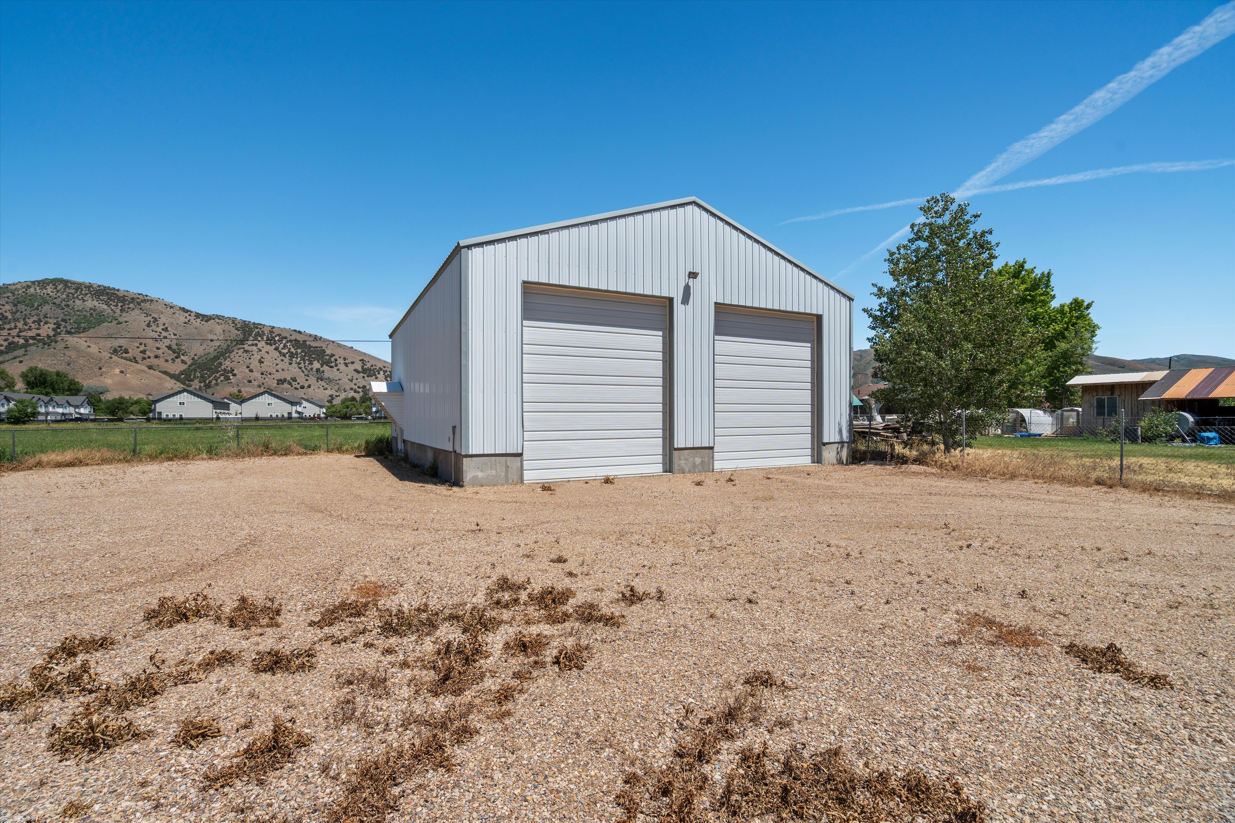 Metal pole barn featuring a gable roof, two overhead garage doors, exterior lighting fixtures, and a gravel lot