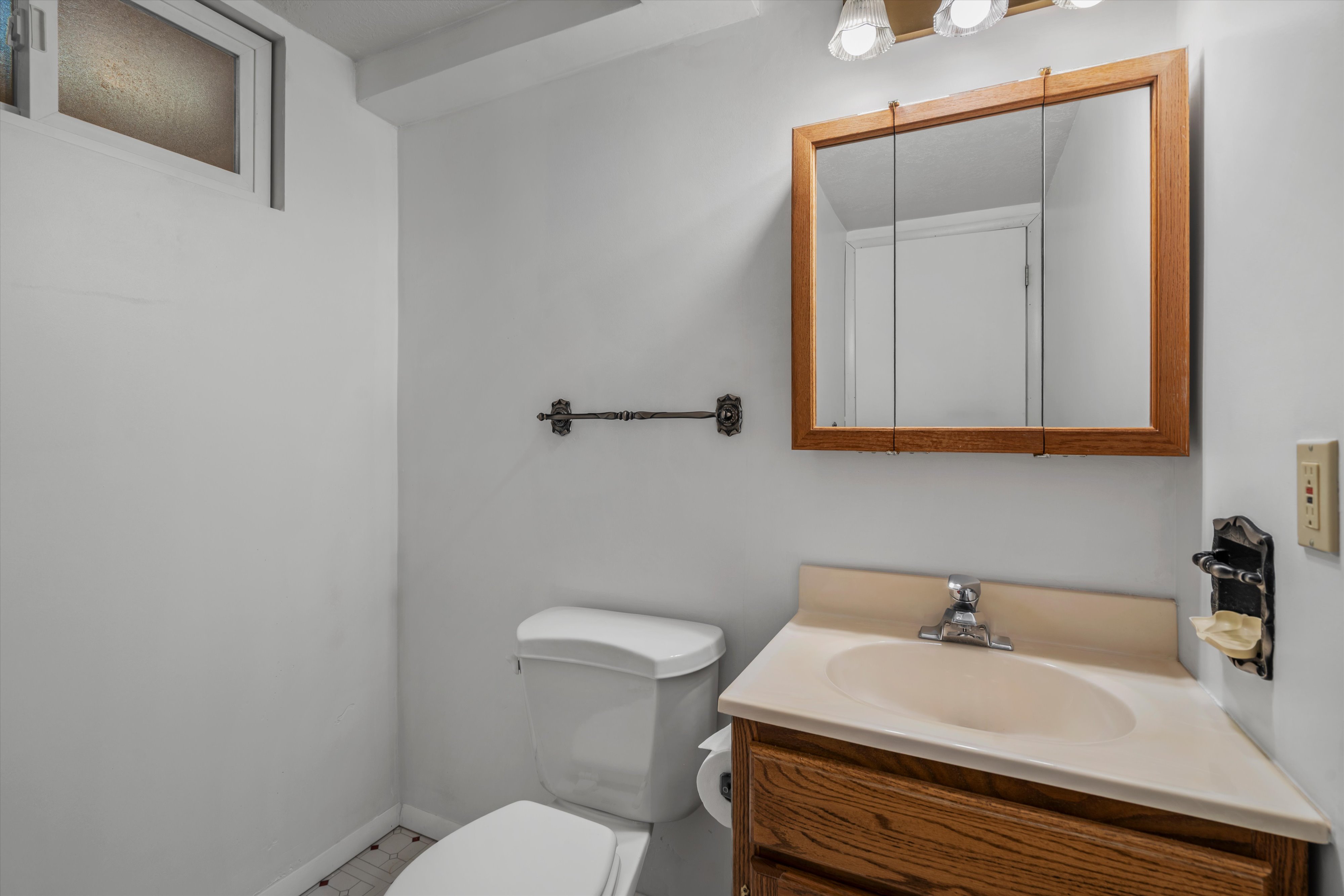 Compact bathroom featuring a corner vanity with a light-toned countertop, a wood-finish medicine cabinet, and a window with frosted glass