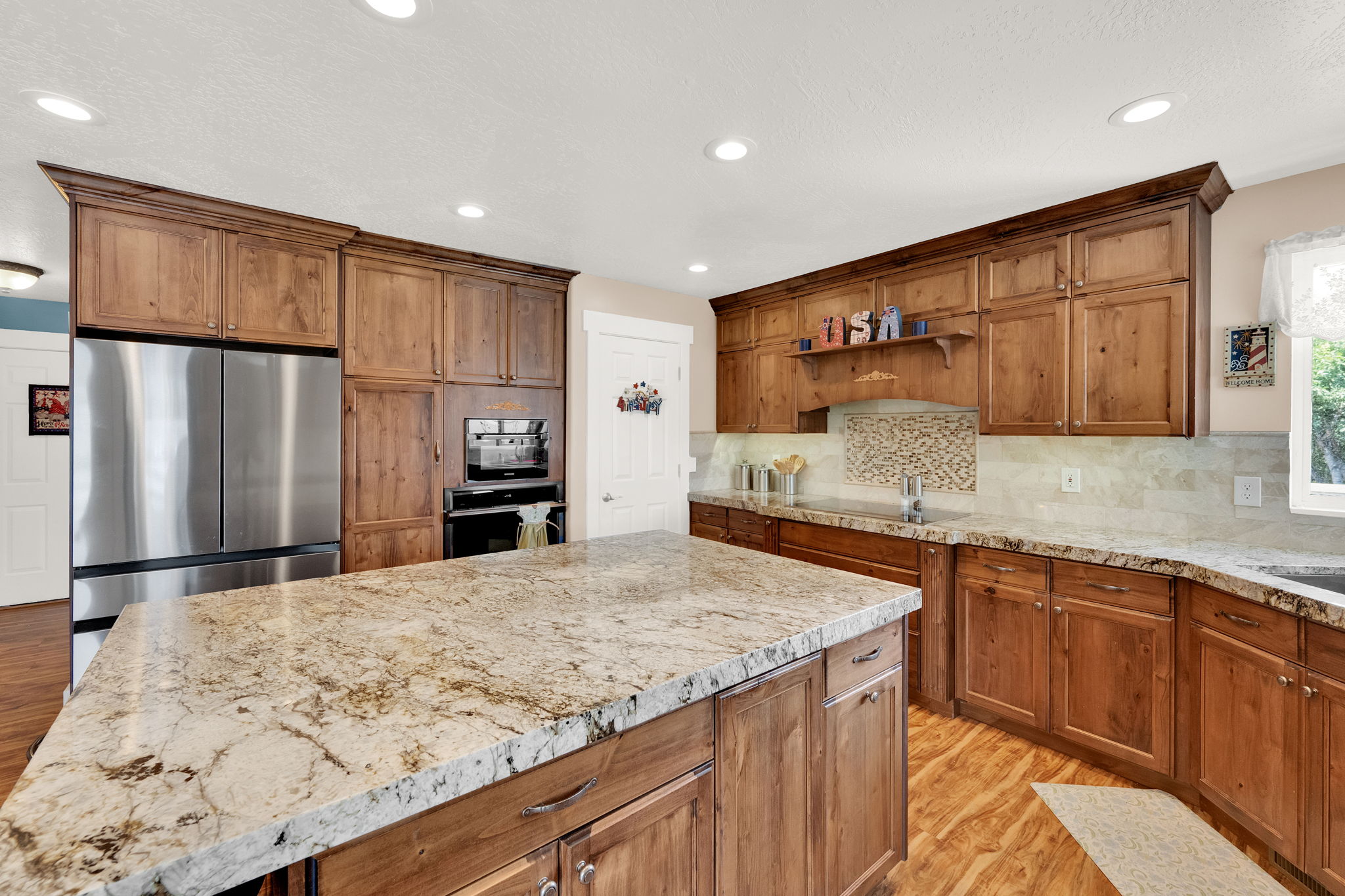 Kitchen featuring a large central island with a stone countertop, extensive wood cabinetry, stainless steel appliances, and wood-finish flooring