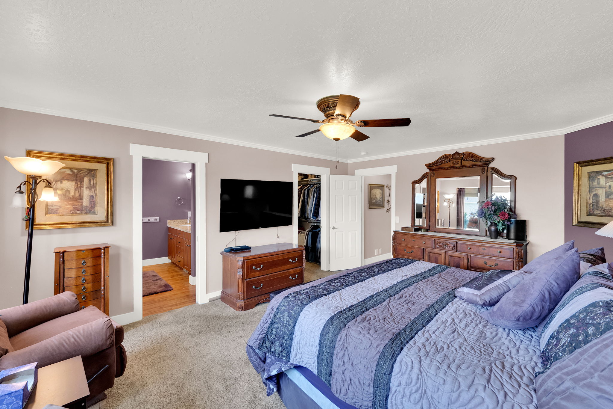 Carpeted room featuring a ceiling fan with integrated lighting, white trim, and a doorway leading to a bathroom with wood-finish flooring and a vanity with a light-colored countertop