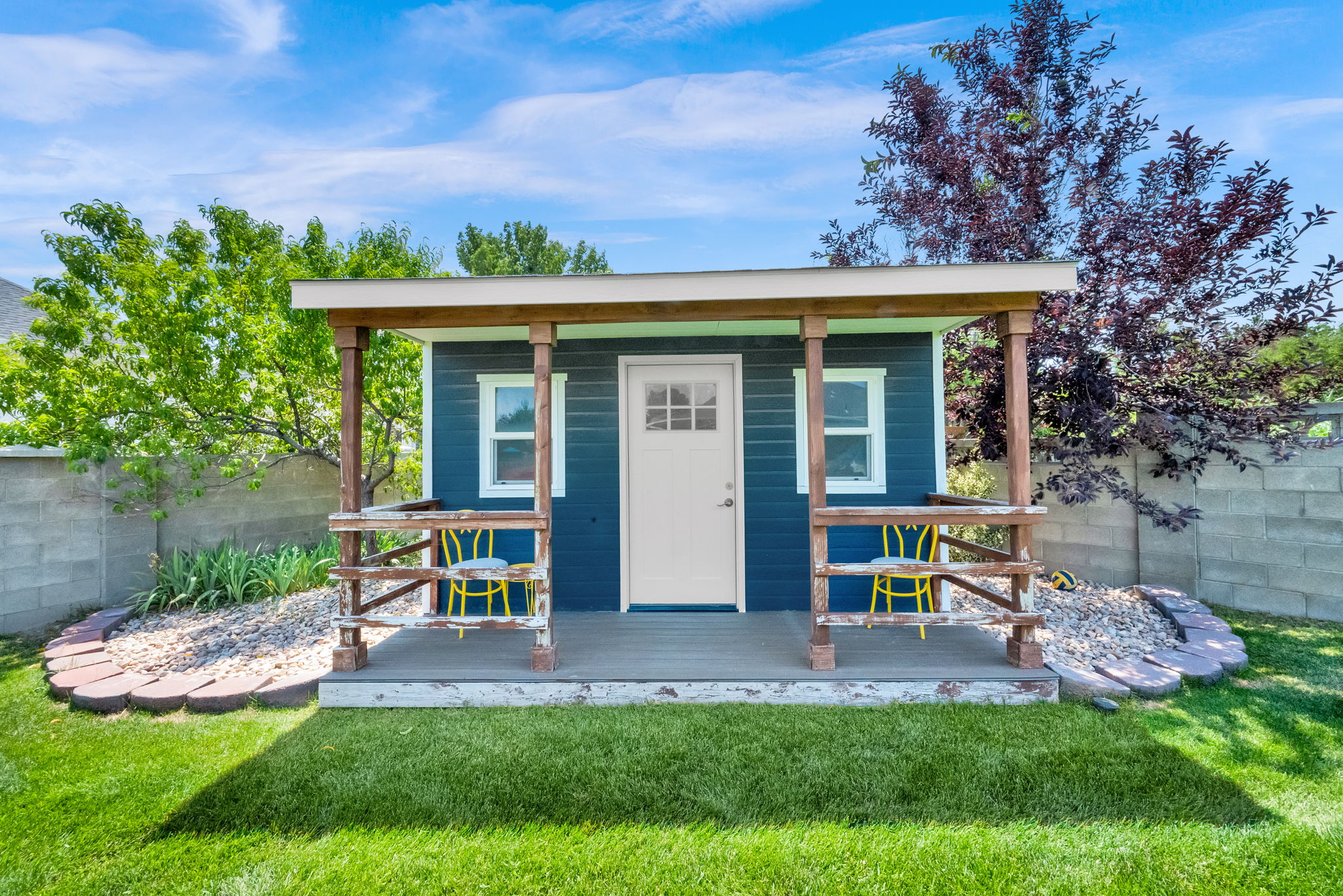 Detached structure with a covered porch featuring a white entry door, two windows, and blue siding