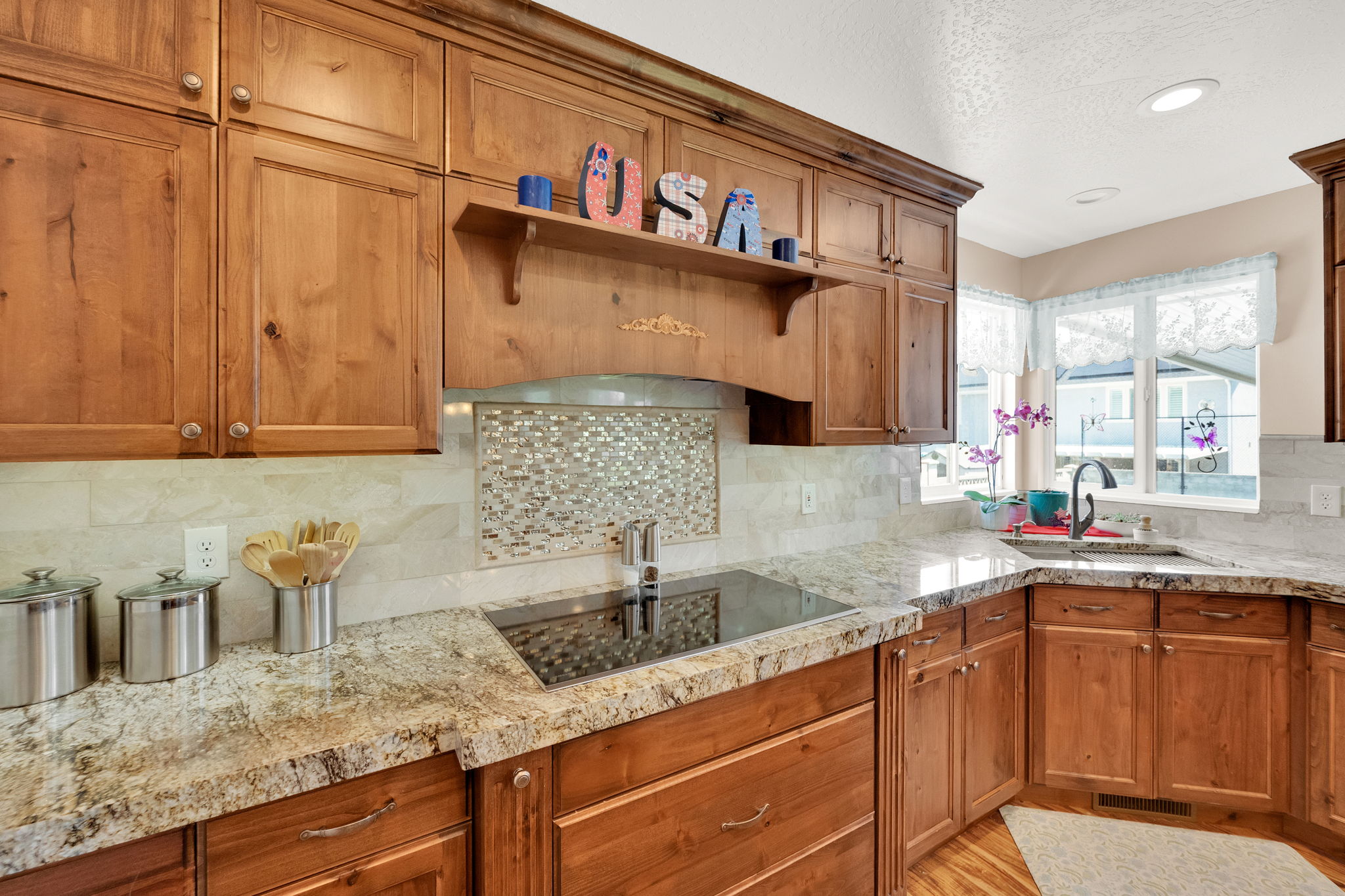 Kitchen featuring wood cabinetry, light-toned granite countertops, a mosaic tile backsplash, and an integrated cooktop