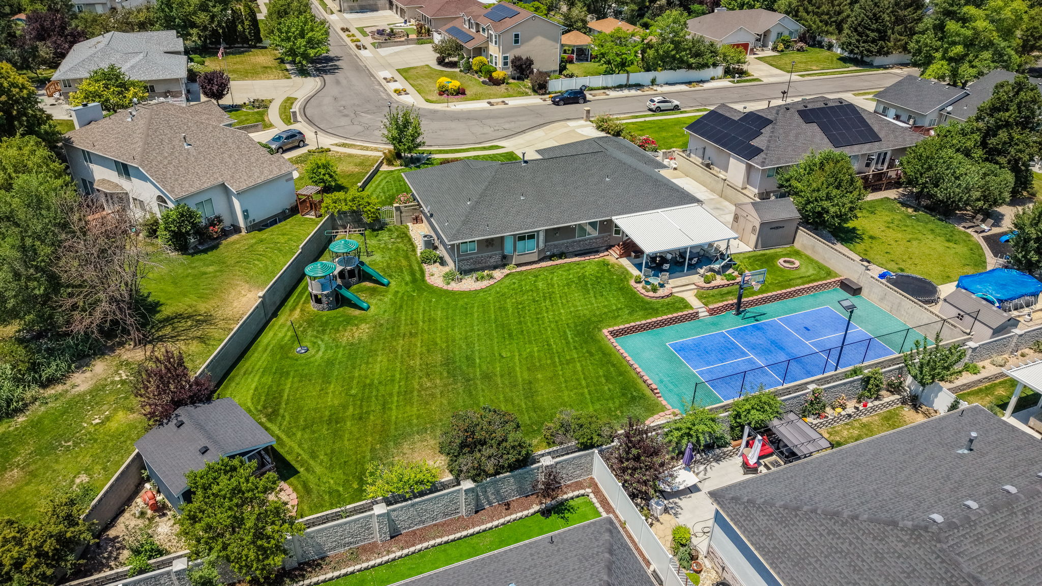 Expansive green lawn with a sports court, covered patio, and mature landscaping