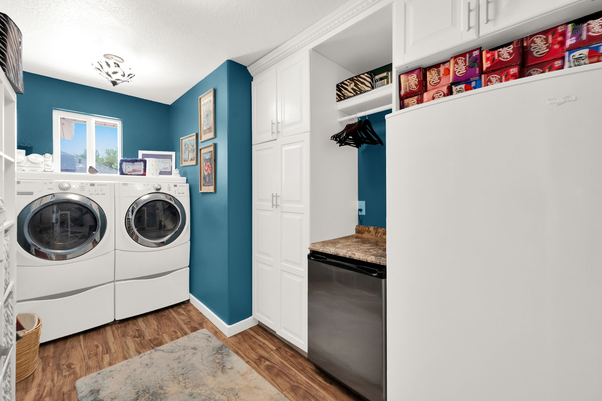 Dedicated laundry area featuring wood-finish flooring, white built-in cabinetry, a built-in hanging rod, and a window for natural light
